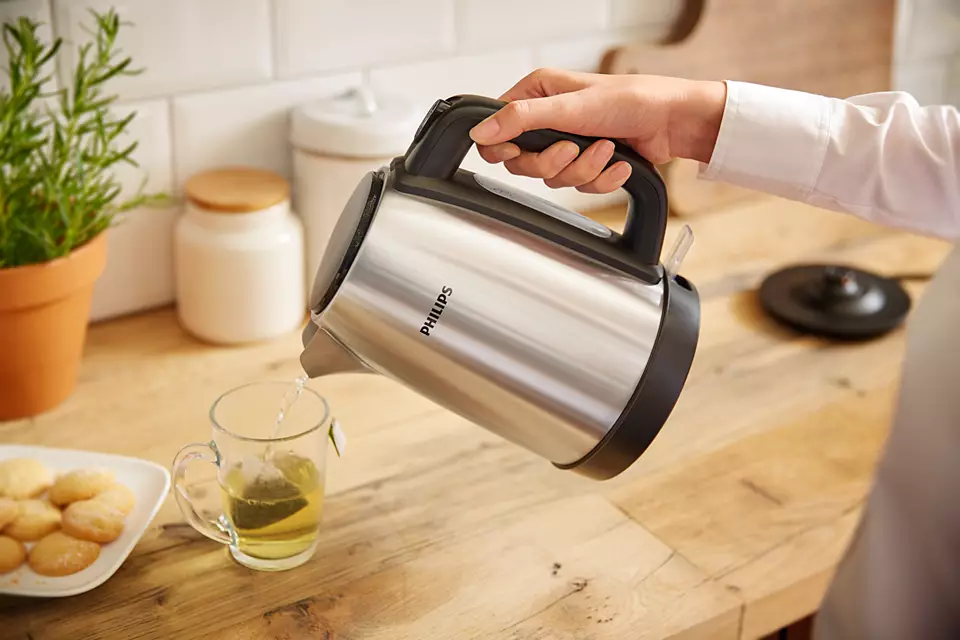 Egy kéz vizet önt a Philips vízforralóból egy csésze teába, fa felületen.