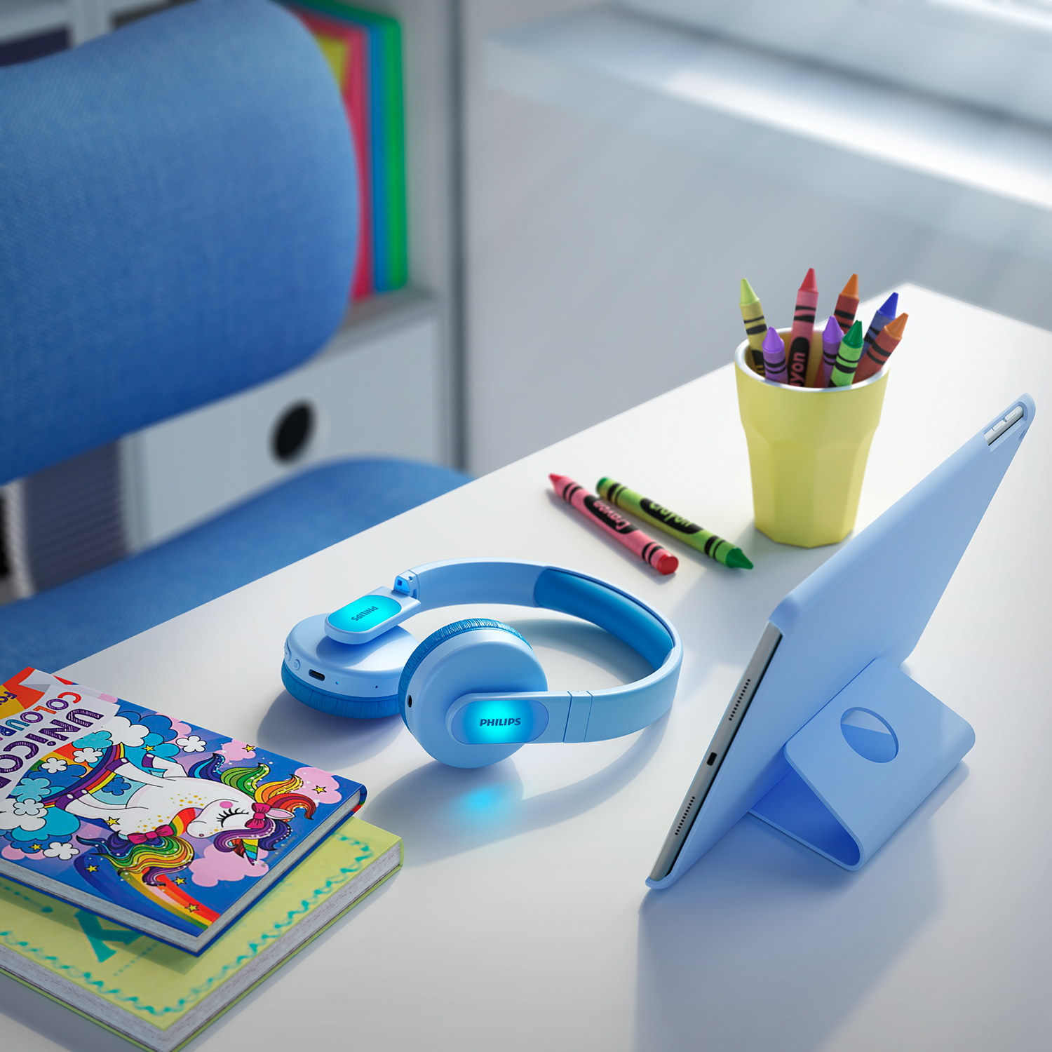 Blauwe koptelefoon, tablet en kleurpotloden op een bureau. Er is ook een eenhoorn kleurboek.