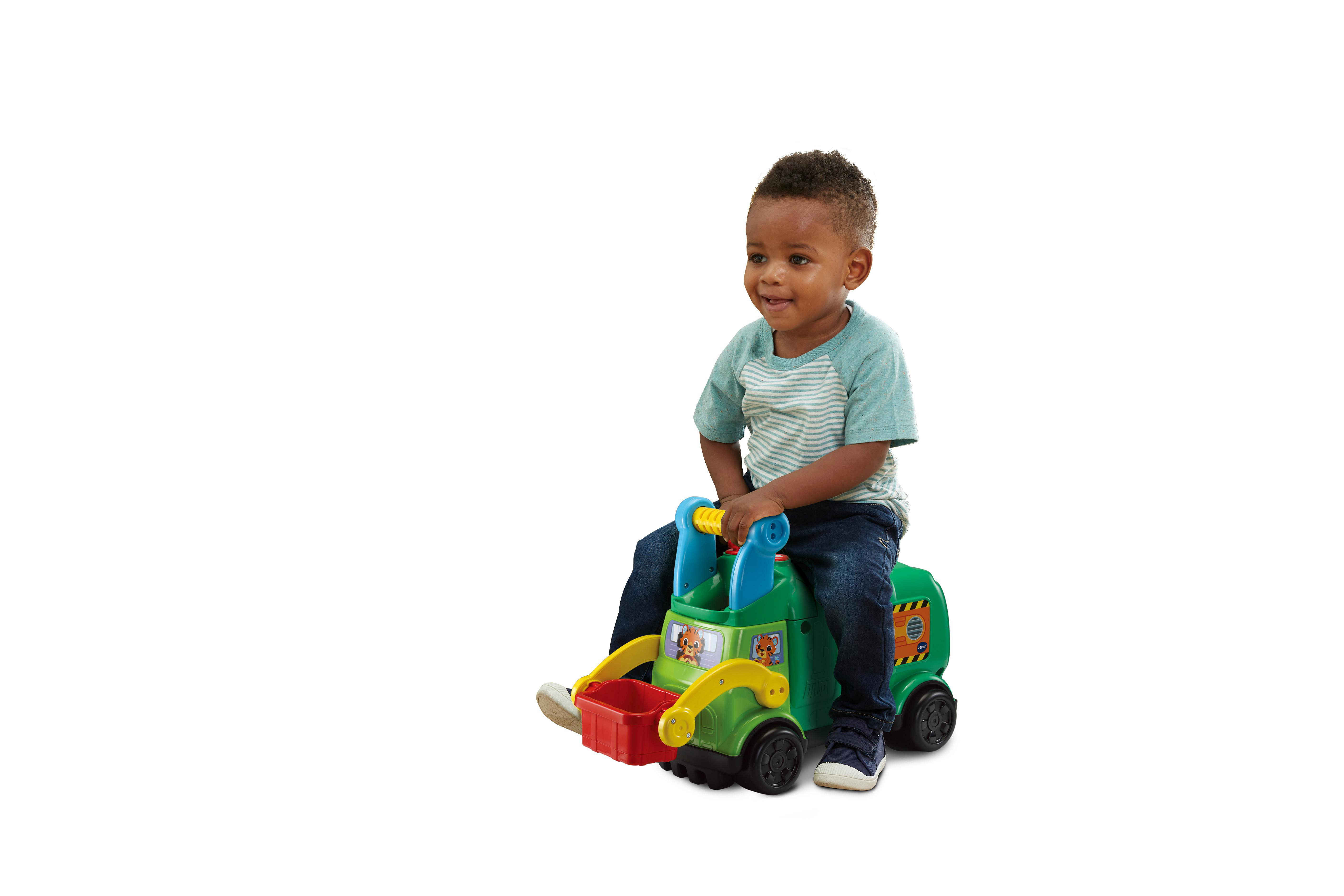 Ein kleiner Junge sitzt auf einem grünen Spielzeug-LKW. Der LKW hat einen roten Behälter.