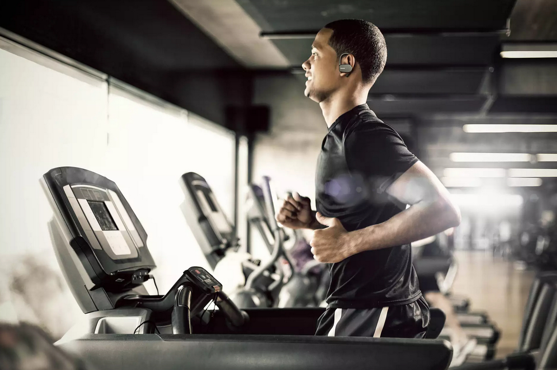 Mann läuft auf Laufband im Fitnessstudio mit Ohrhörern. Verschwommener Hintergrund.
