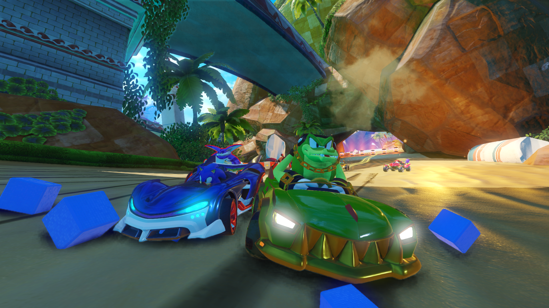 Sonic und Vector rasen in Karts auf einer Strandstrecke mit Felsformationen und blauen Blöcken.