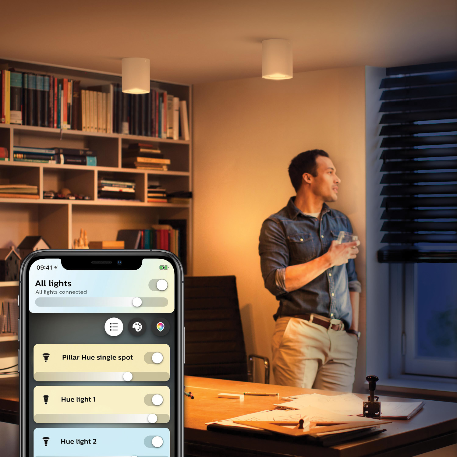 Un homme regarde par la fenêtre. Un téléphone avec une application contrôle l'éclairage de la pièce.