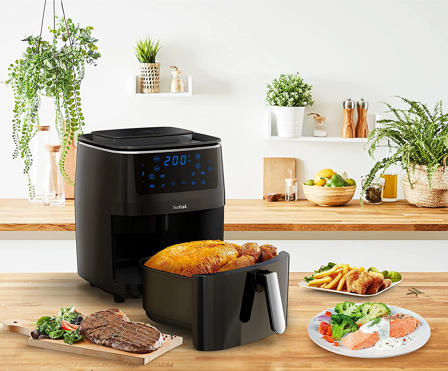Fekete légsütő sült csirkével, steakkel, krumplival és zöldségekkel az asztalon.