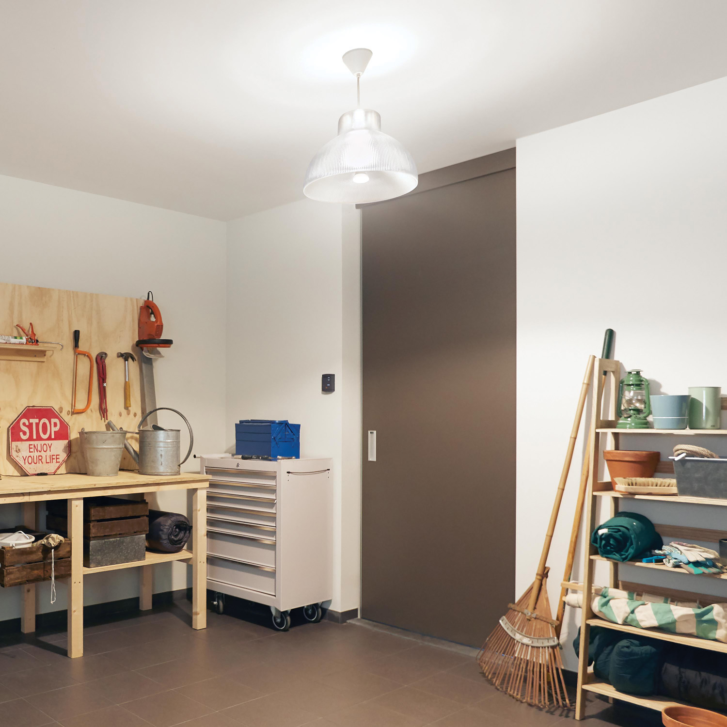 Garage interior with tools on wall, workbench, cabinet, sliding door, and shelves with items.