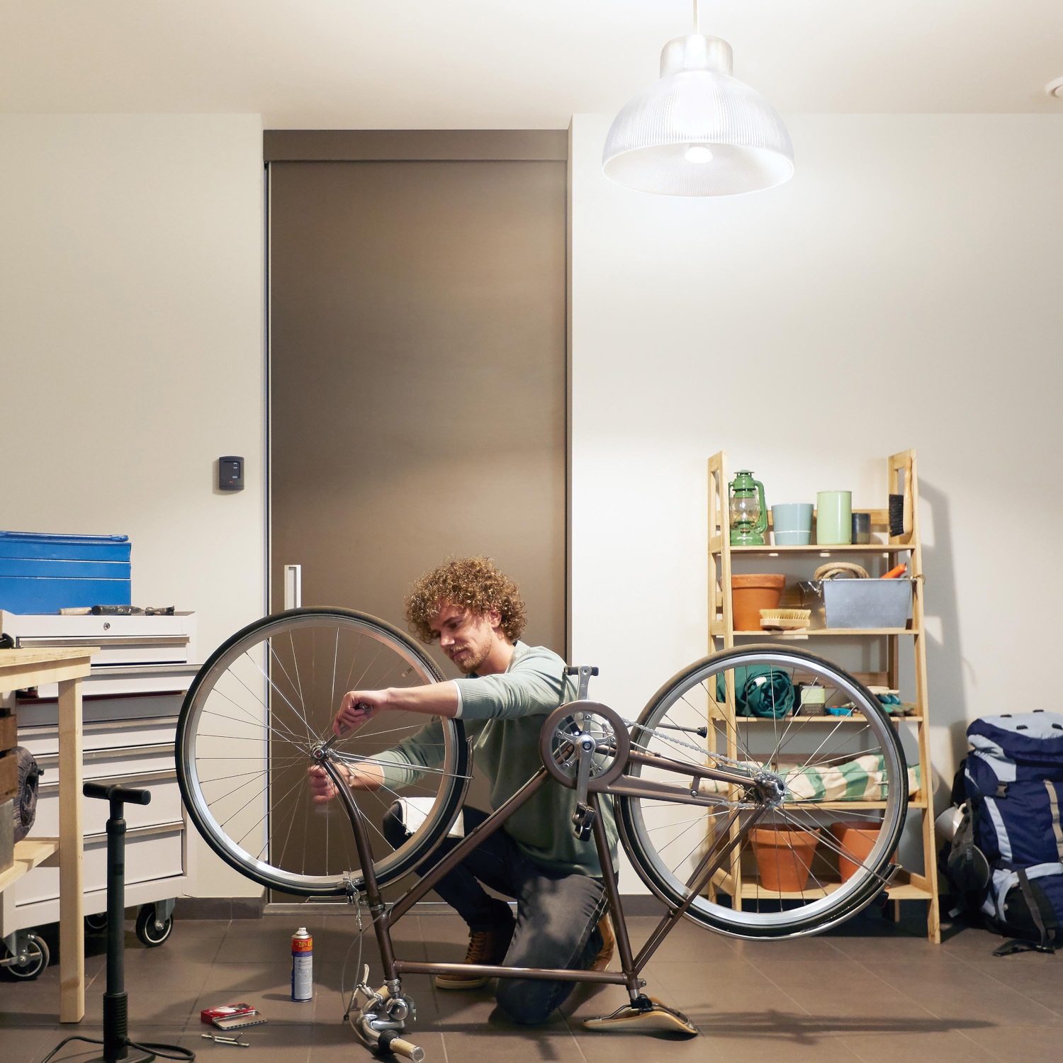 A man working on a bicycle in a garage. Tools and equipment are nearby.