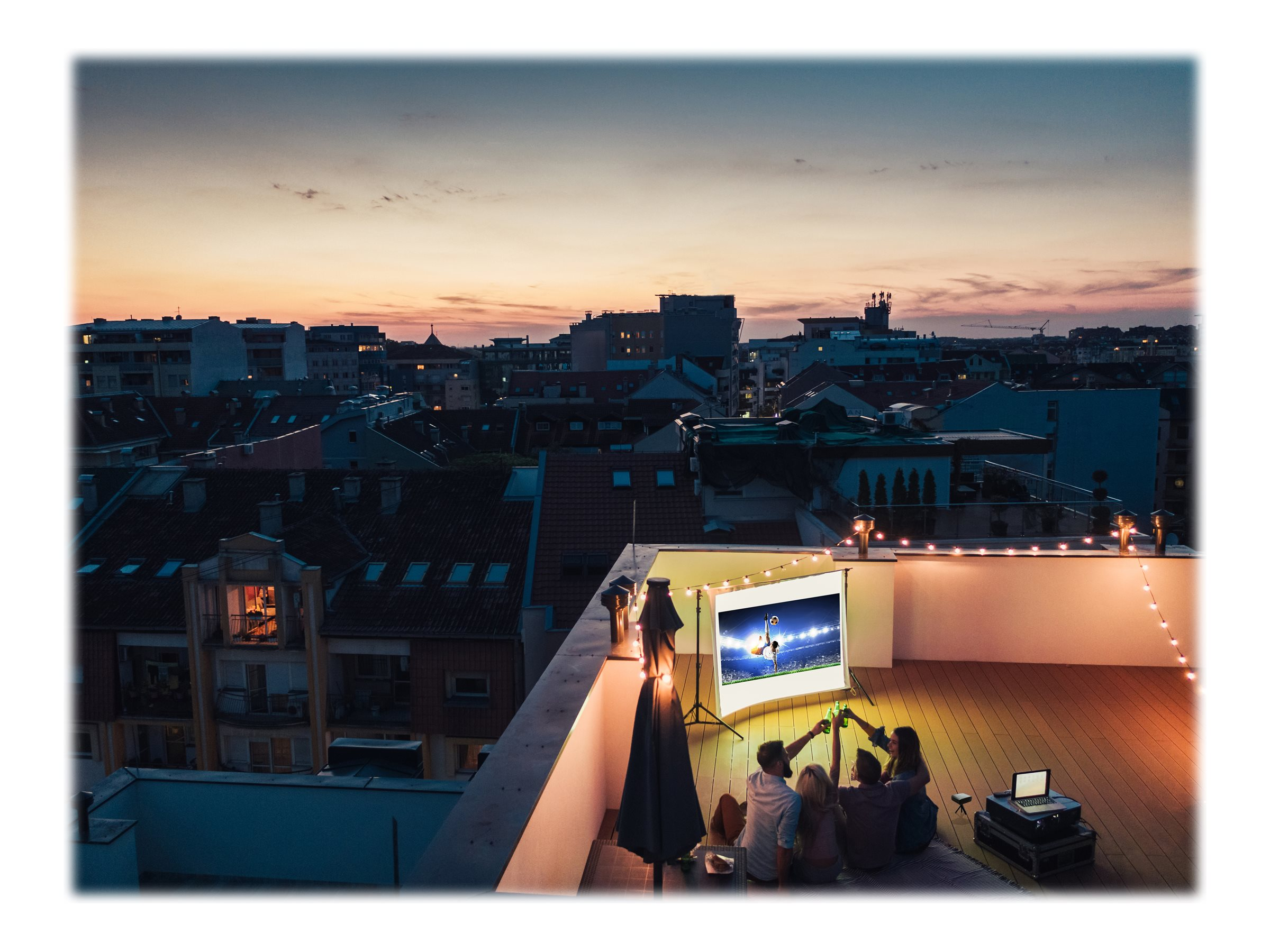 Mensen kijken naar een film die op een scherm op een dak wordt geprojecteerd bij zonsondergang.
