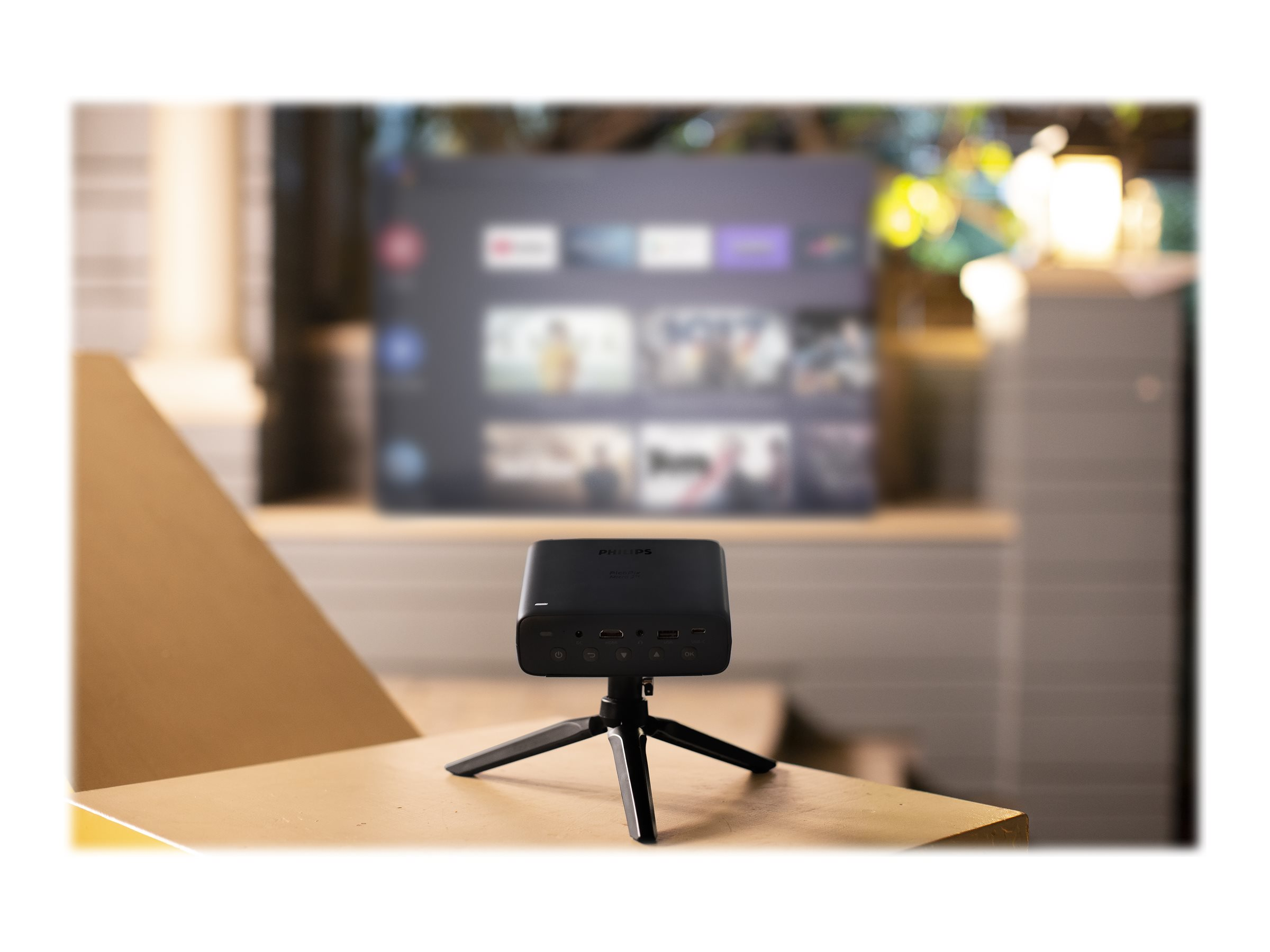 Een zwarte projector op een statief, met een scherm op de achtergrond, op een houten tafel.