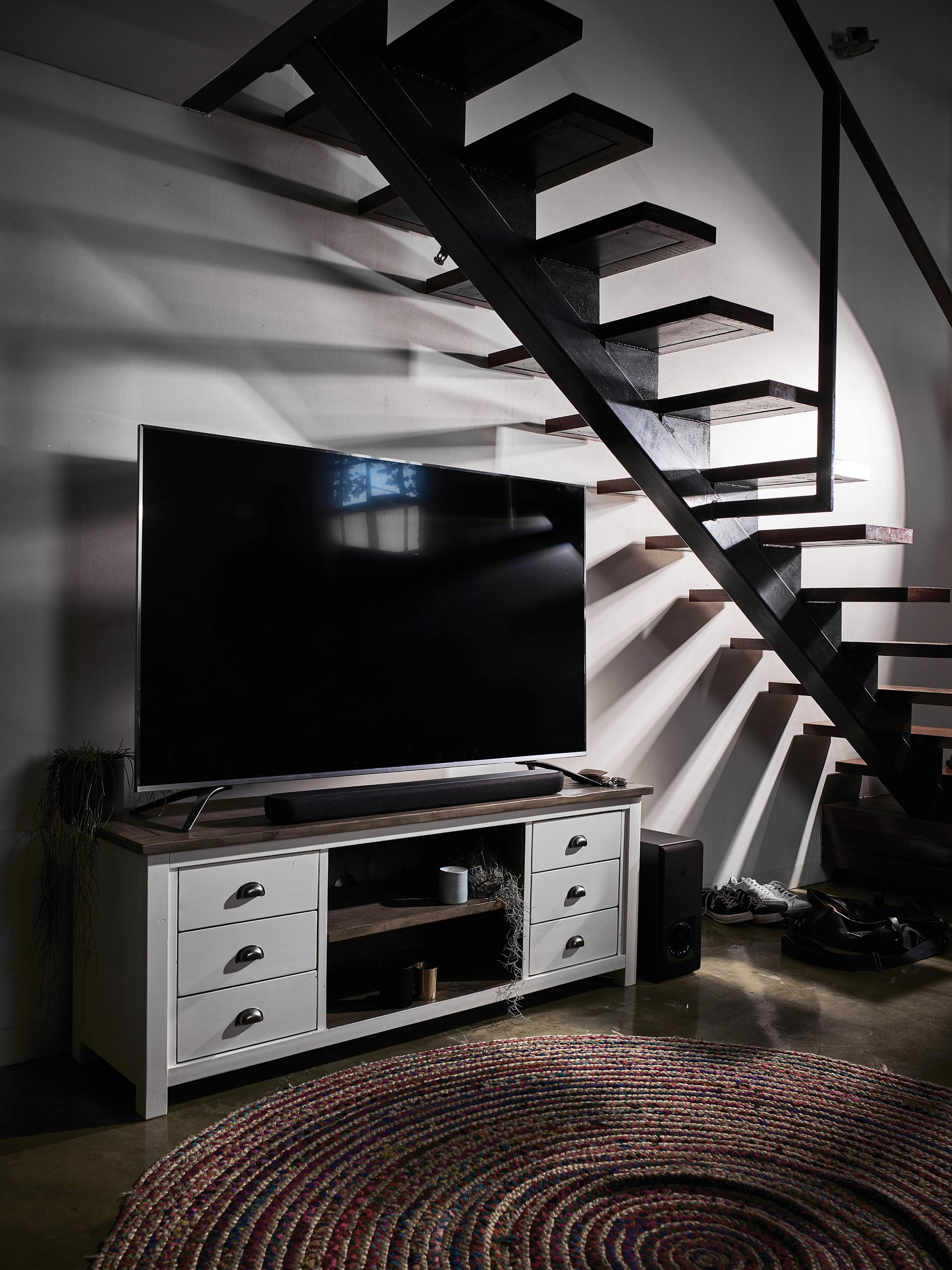 Modernes Wohnzimmer. Ein großer Fernseher, ein Teppich und eine Treppe sind sichtbar.