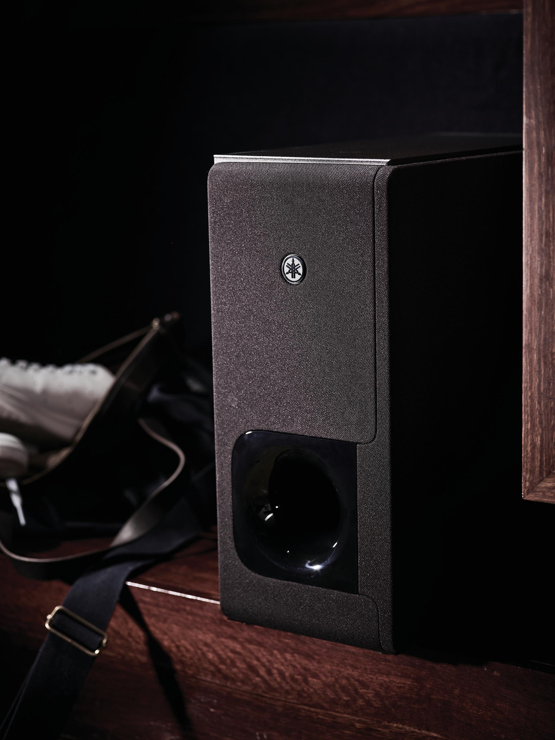 Eine schwarze Yamaha Soundbar steht auf einer Holzoberfläche. Eine Handtasche ist links von der Bar sichtbar.