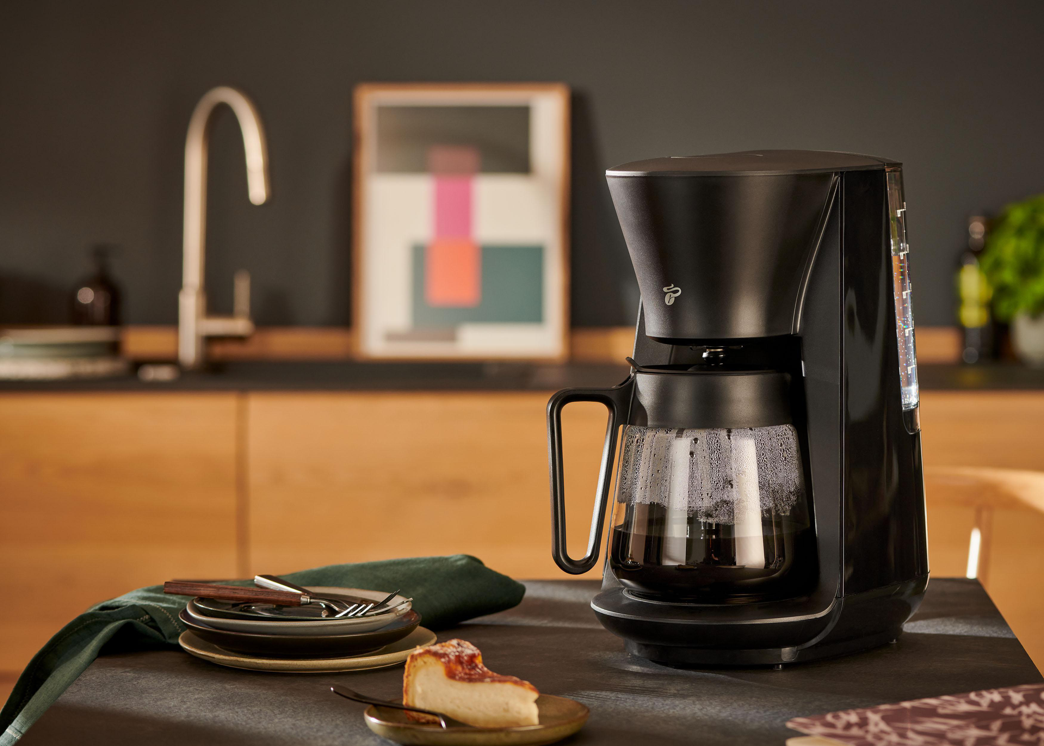 Schwarze Kaffeemaschine beim Brühen von Kaffee. Glaskaraffe sichtbar. Küchenhintergrund.