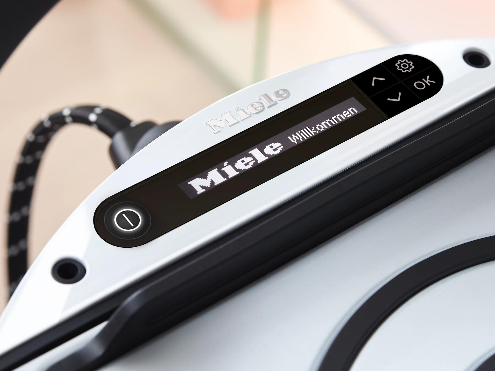 Nahaufnahme eines weißen Miele-Geräts mit einem Bildschirm, der 'Miele Willkommen' anzeigt.
