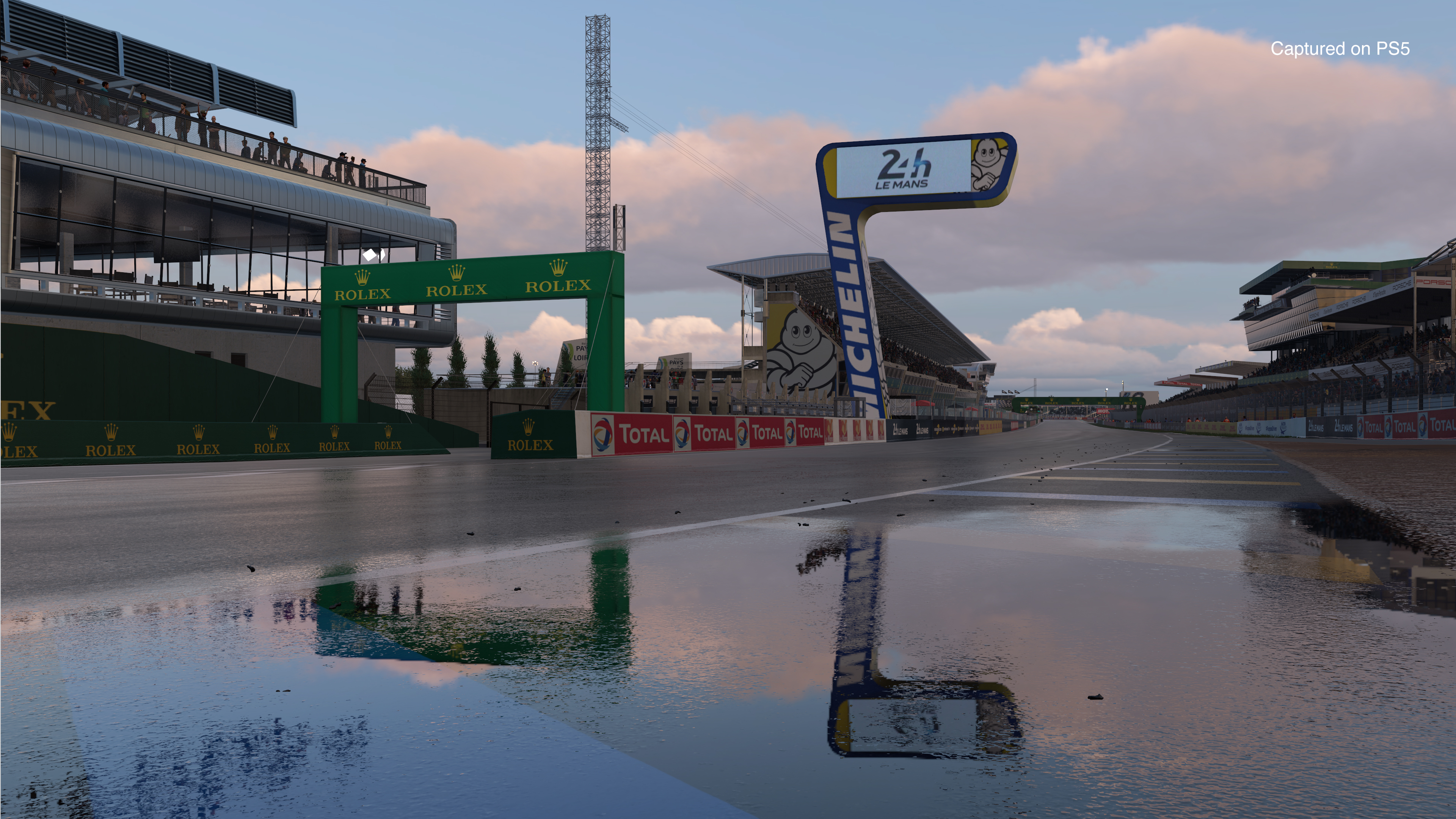 A racetrack with wet asphalt. A sign for Le Mans is visible.