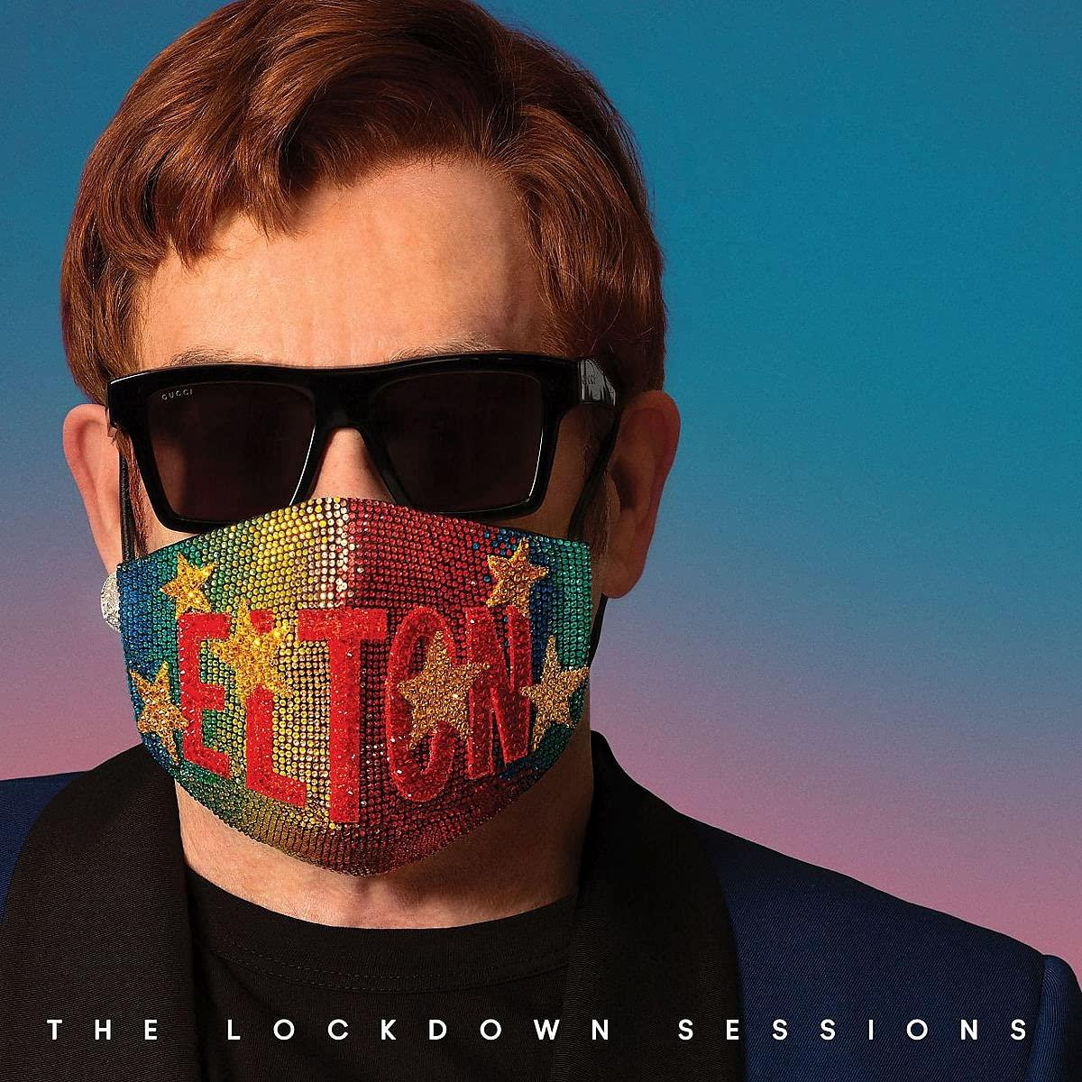 Elton John napszemüveget visel, és egy strasszokkal díszített maszkot, rajta az „ELTON” felirattal. A háttér kék és rózsaszín átmenet.