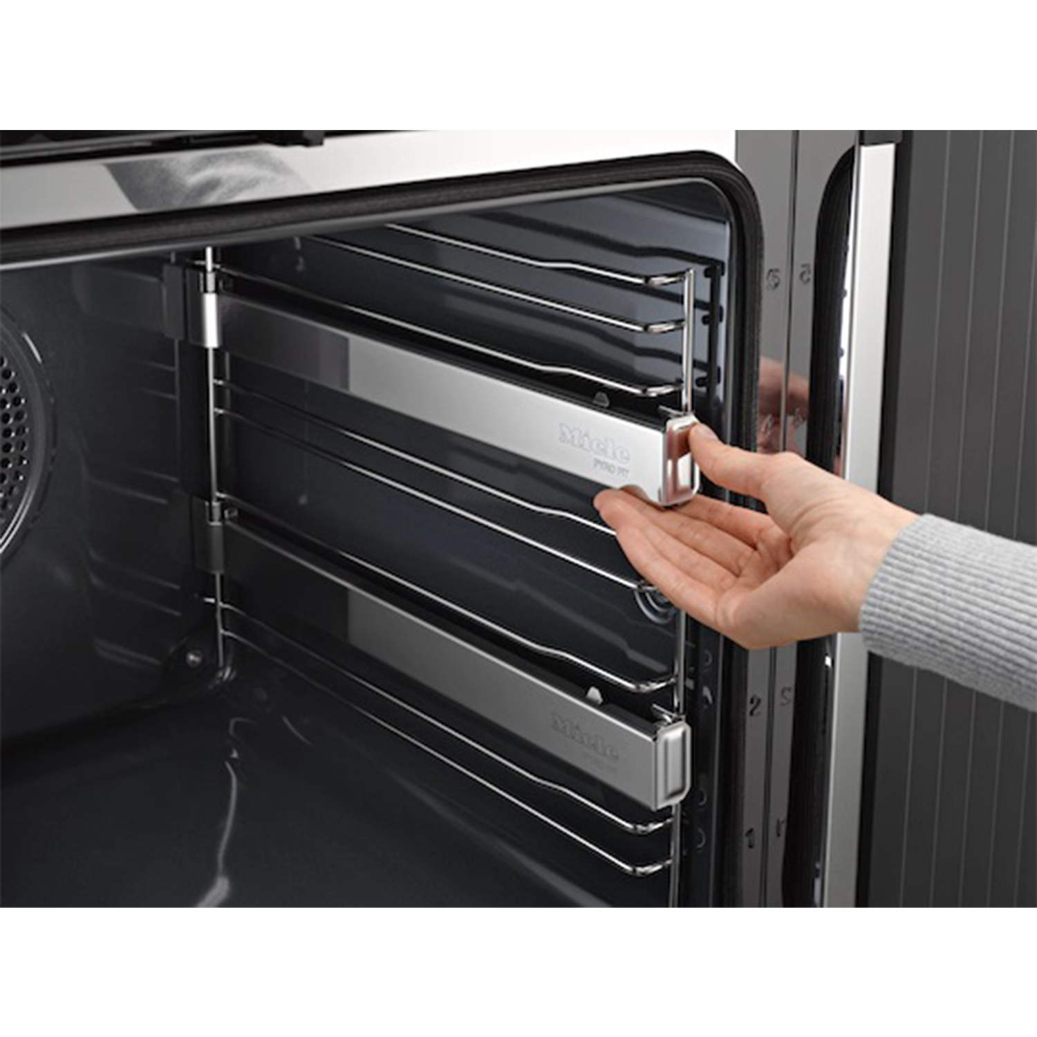 Una mano estrae una griglia dall'interno di un forno in acciaio inox con il marchio Miele.