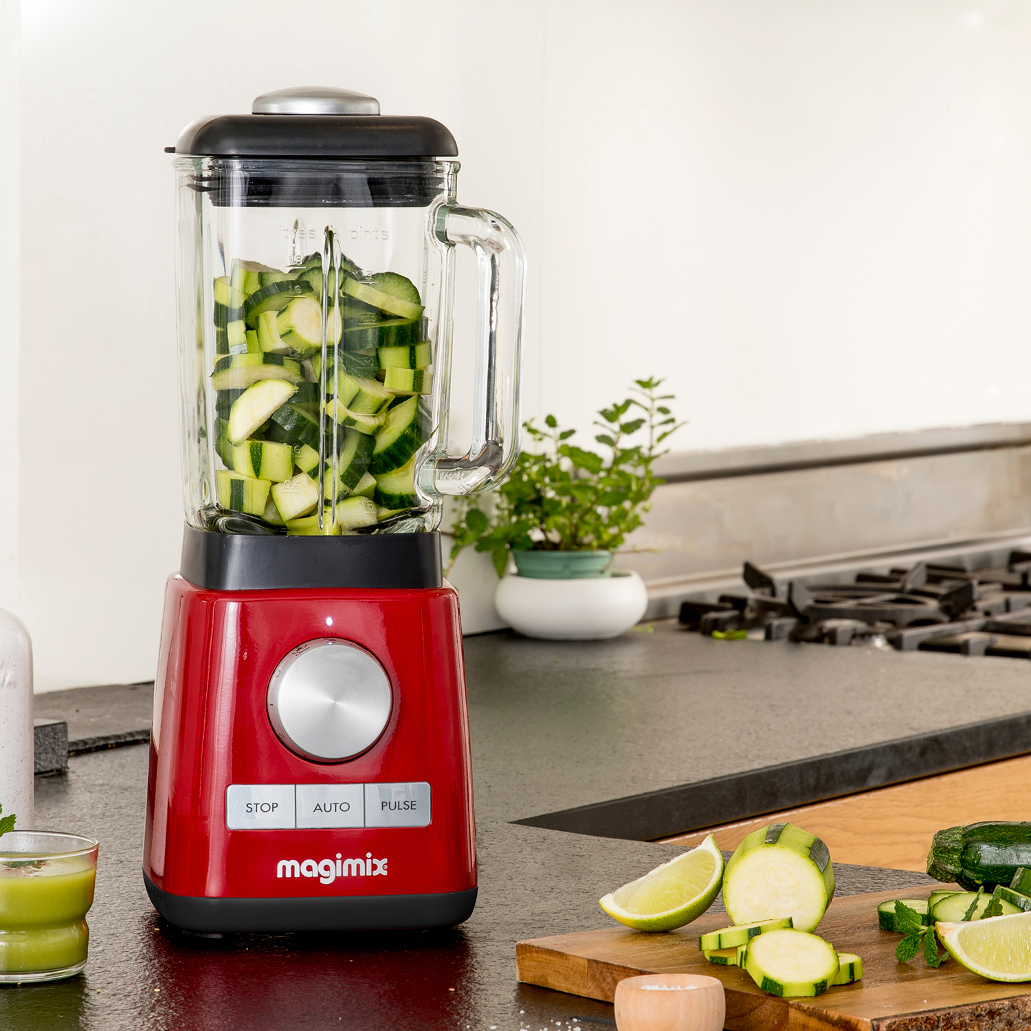 Een rode blender met courgette erin en ingrediënten op een aanrecht.