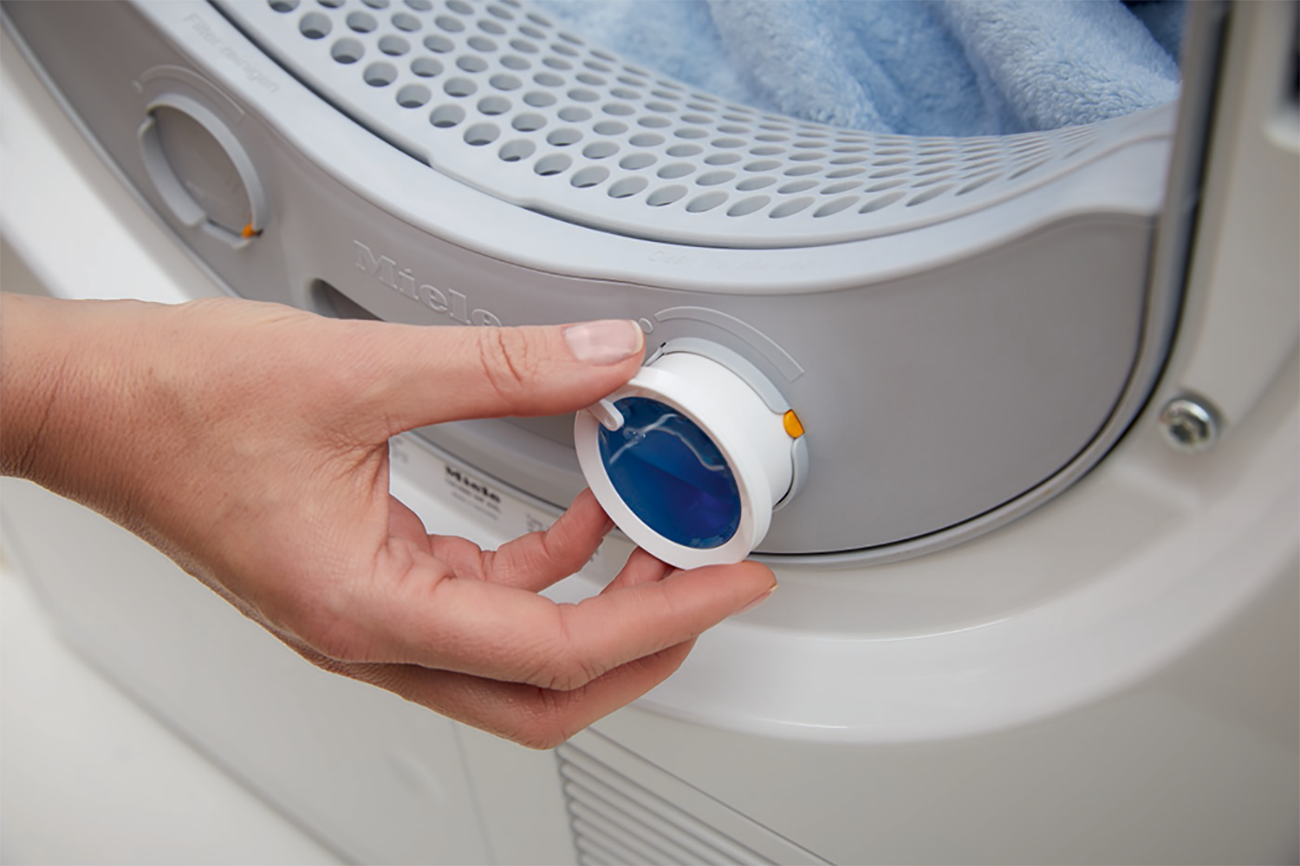Een hand draait aan de bedieningsknop van een droger. De knop is wit en blauw.
