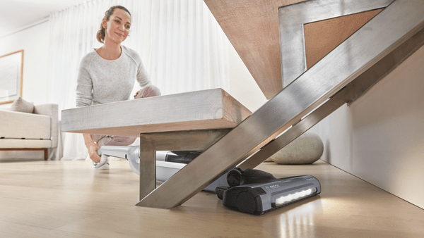 Eine Frau in der Nähe einer Treppe, mit einem Staubsauger unter der Treppe, der den Boden reinigt.
