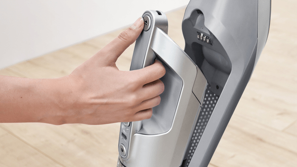 Eine Hand drückt einen Knopf an einem grauen Staubsauger.