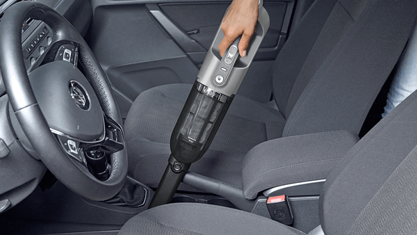 Eine Hand benutzt einen schnurlosen Staubsauger in einem Auto und reinigt die Sitze.