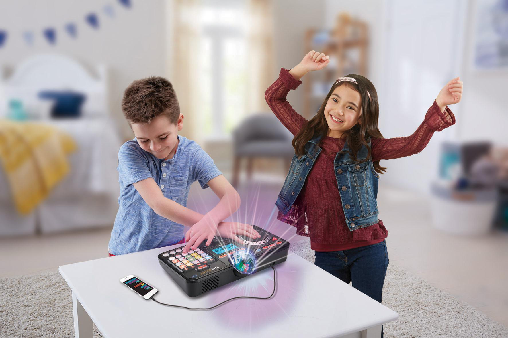 Zwei Kinder spielen mit einem DJ-Mixer-Spielzeug auf einem weißen Tisch in einem Raum.