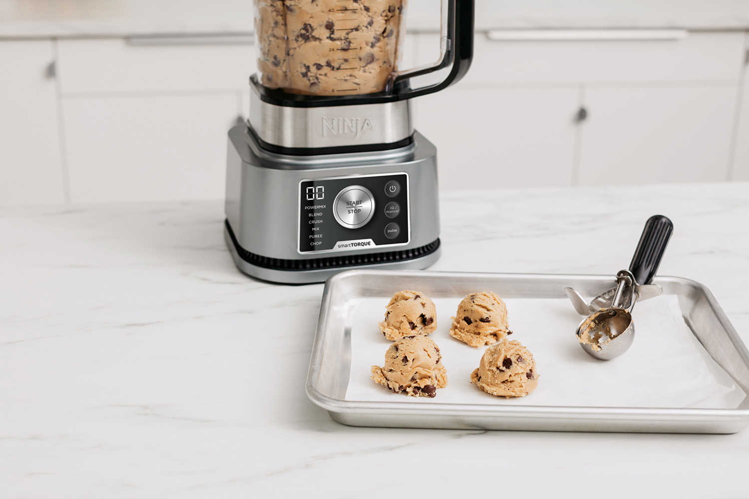 Keukenmachine maakt koekjesdeeg. Deegballen op een bakplaat.