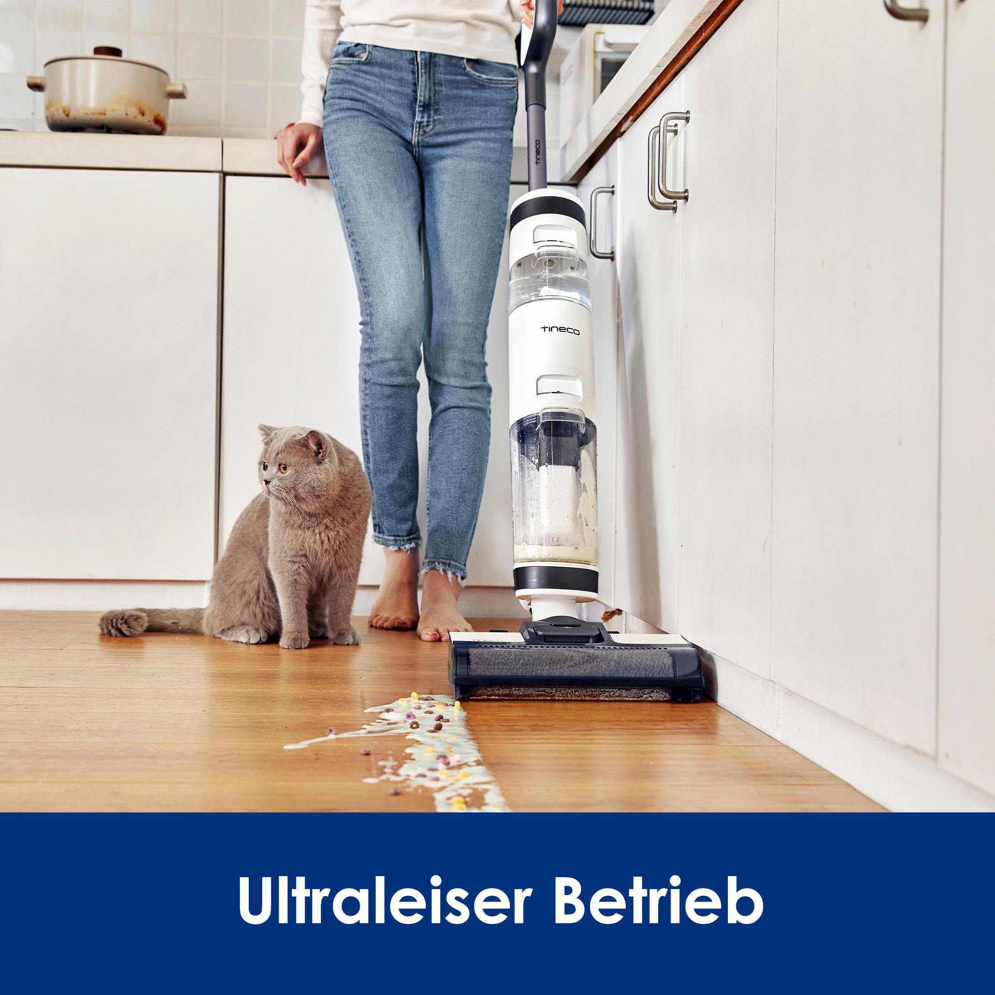 Frau benutzt einen weiß-schwarzen Bodenreiniger. Eine Katze sitzt in der Nähe.