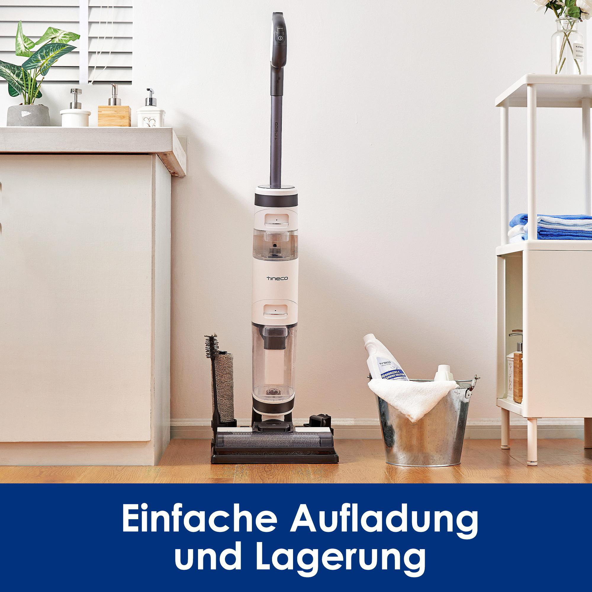 Ein weißer und schwarzer Staubsauger steht vor einer weißen Wand. Zubehör befindet sich links und ein Eimer rechts.