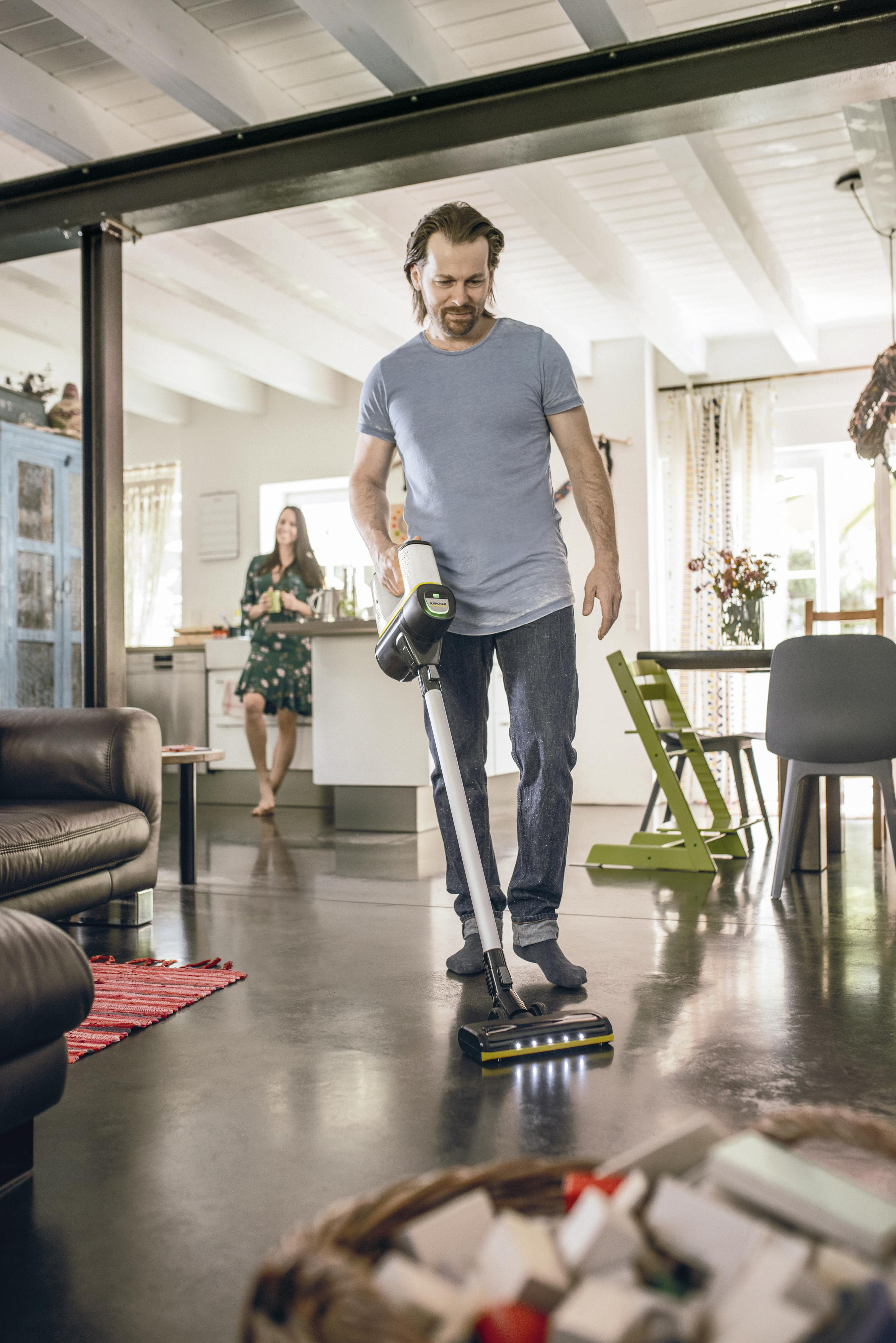 Mann, der ein Wohnzimmer mit einem Kärcher-Reiniger saugt. Frau im Hintergrund.