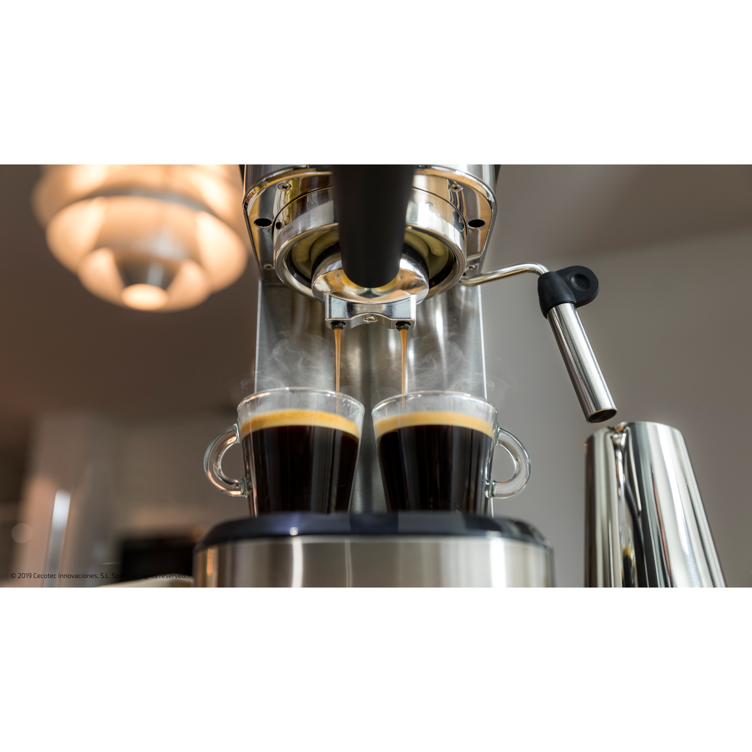 Una máquina de espresso vertiendo café en dos tazas de vidrio. Sale vapor. La luz está encendida.
