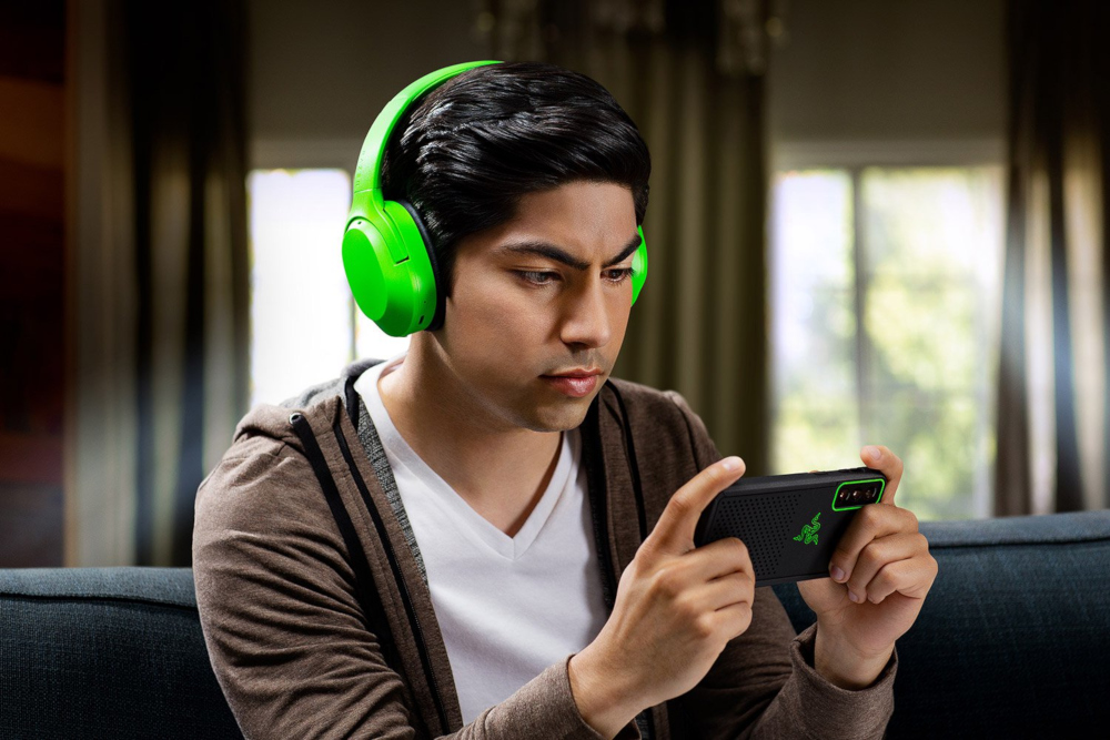 Un homme portant un casque vert jouant à un jeu sur un téléphone en étant assis.