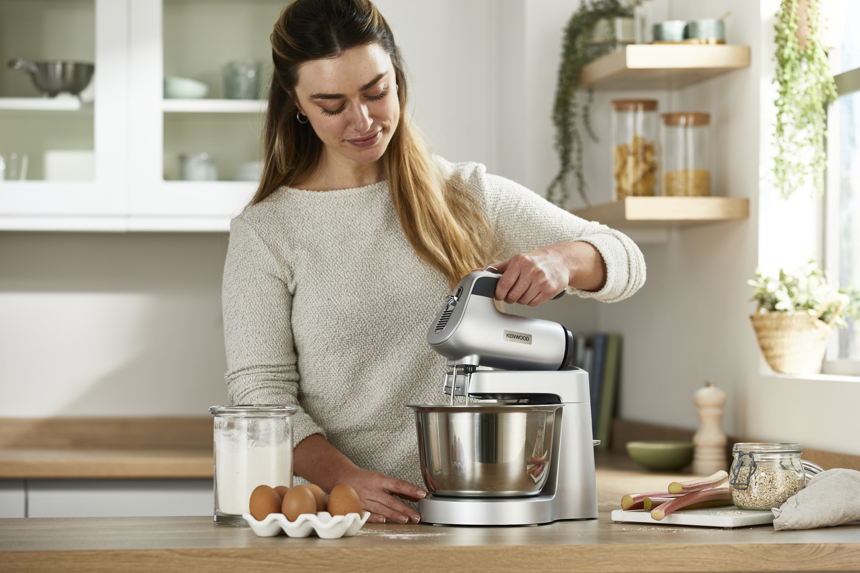 Eine Frau benutzt einen silbernen Küchenmixer. Auf der Theke sind Zutaten.