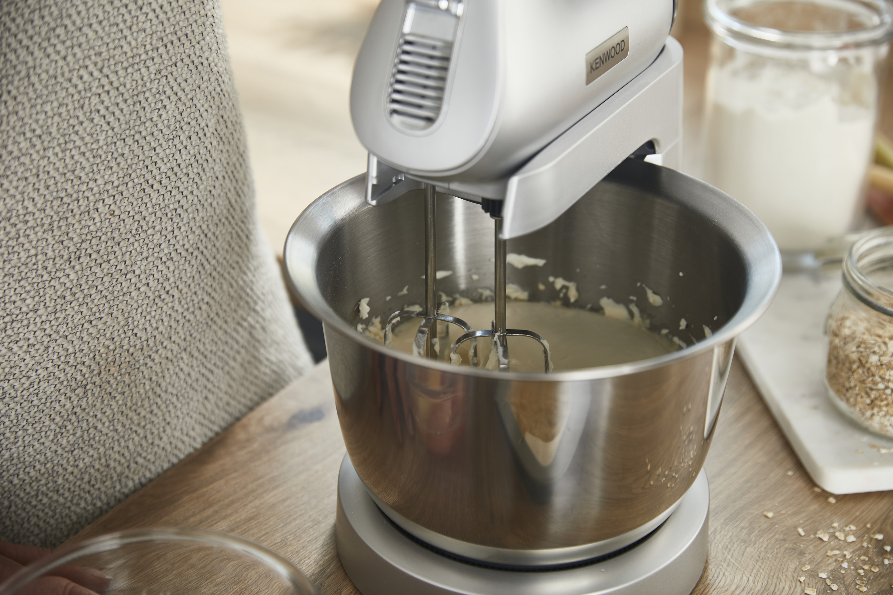 Ein Kenwood-Mixer in Aktion, der Sahne in einer Metallschüssel auf einem Holztisch mit Zutaten verrührt.