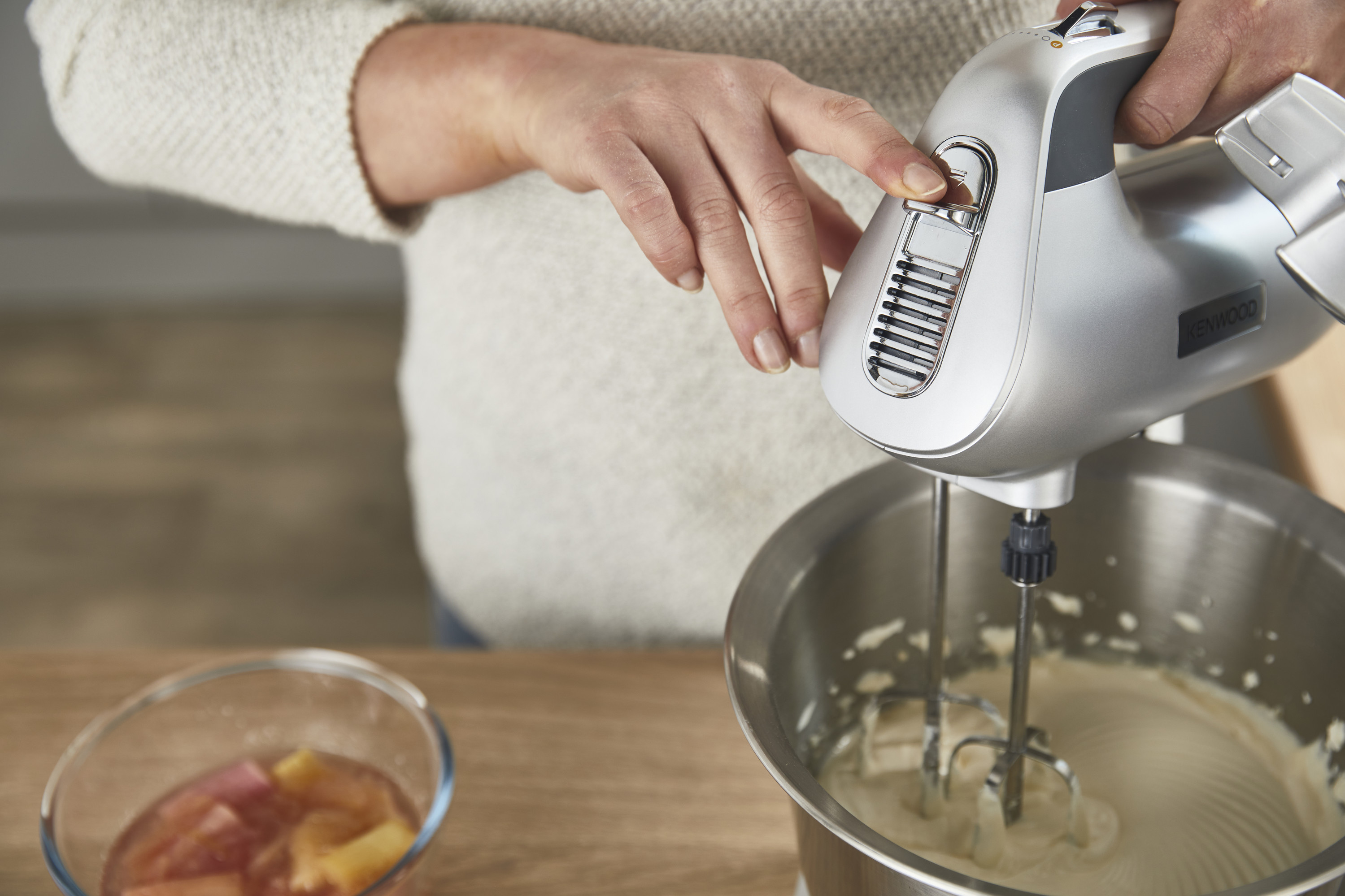Hände benutzen einen silbernen Handmixer. In der Nähe befindet sich eine Schüssel mit Essen.