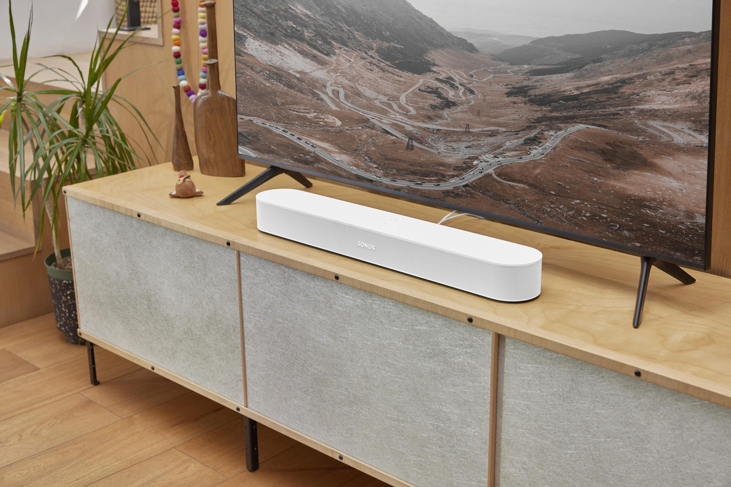 Una soundbar bianca su un mobile in legno sotto una grande TV che mostra un paesaggio.