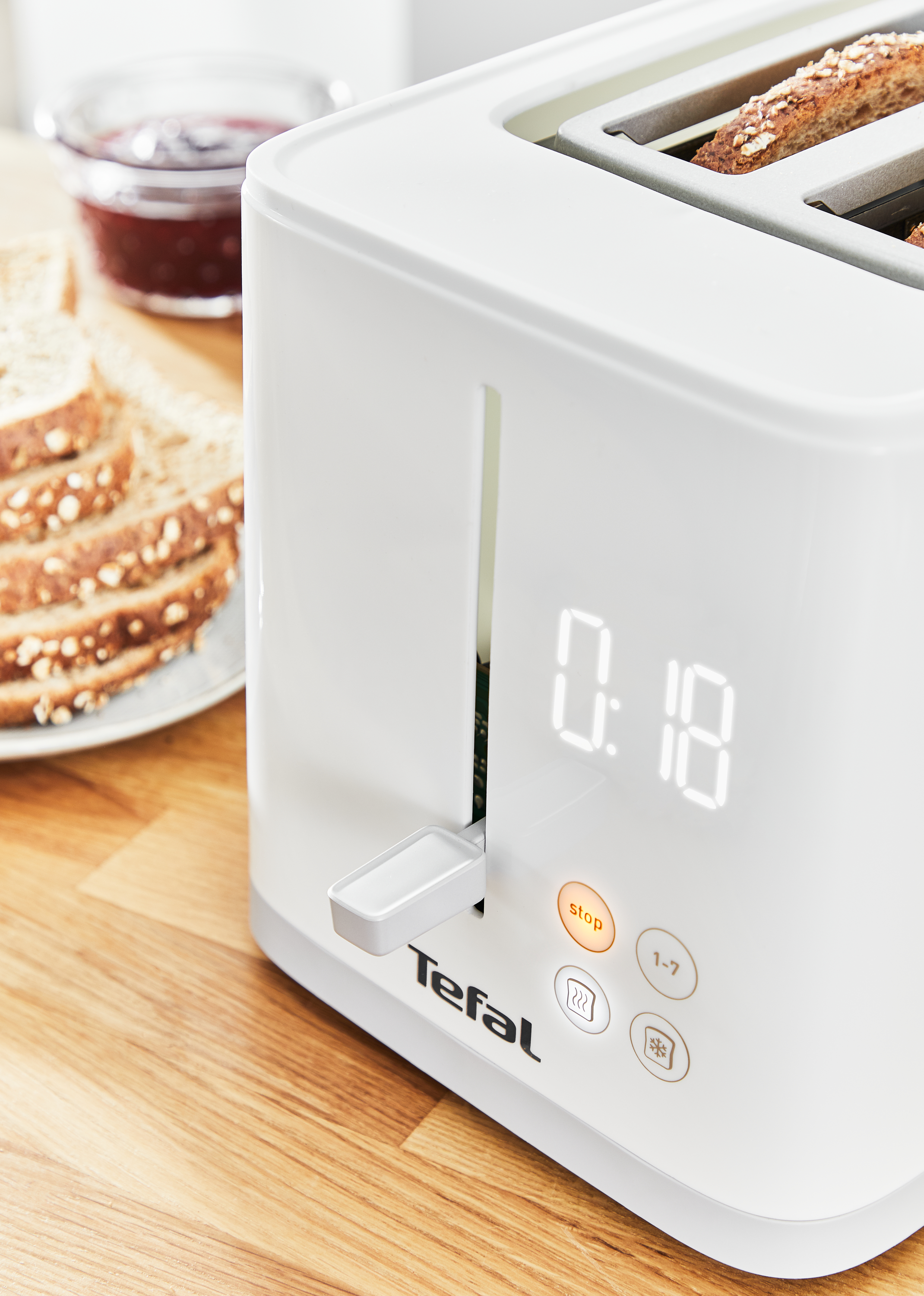Weißer Toaster mit Digitalanzeige, die '0:18' anzeigt. Brot wird getoastet, mit einem Stopp-Knopf sichtbar.