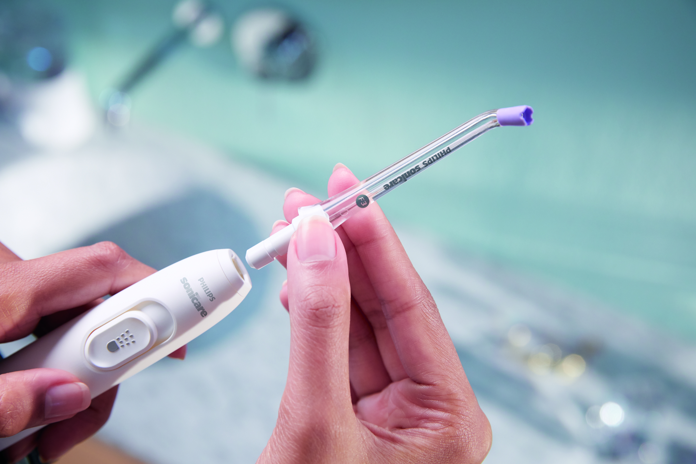 Hände einer Person, die einen weißen Philips Sonicare Wasserflosser zusammenbauen, mit blauem Badezimmerhintergrund.