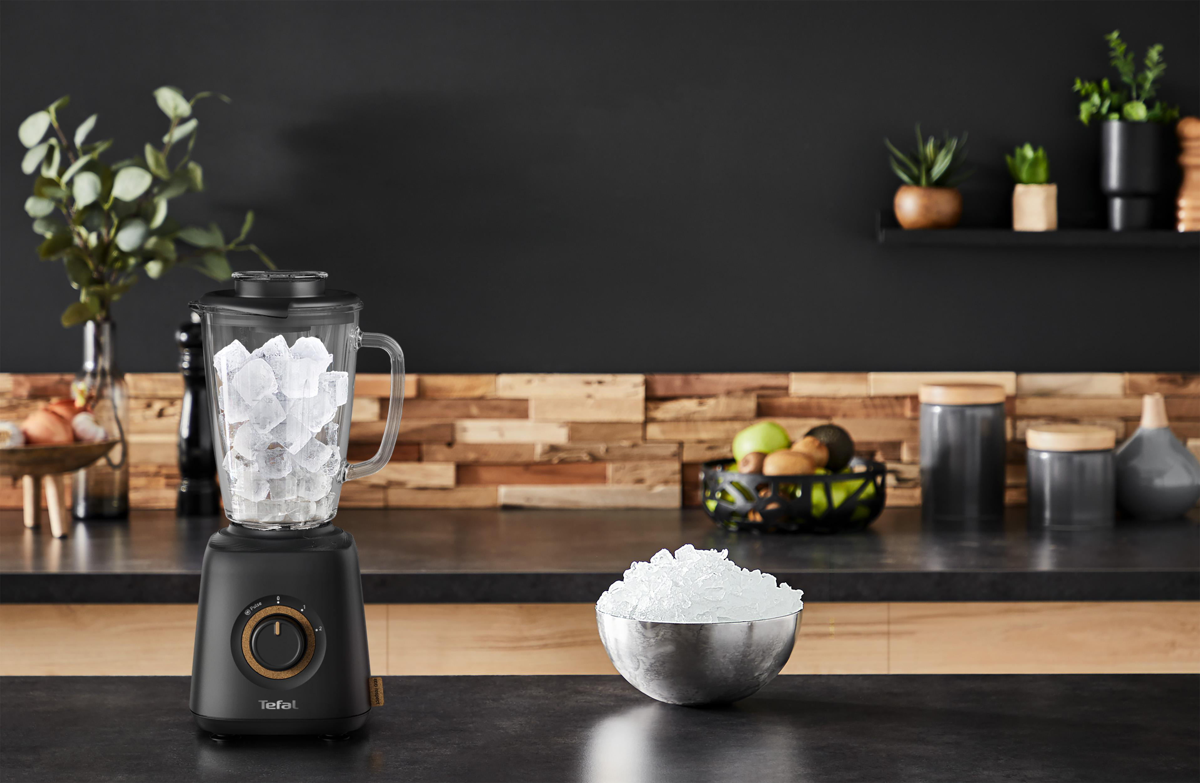 Ein schwarzer Mixer mit Eis im Glas und eine Schüssel mit Eis auf der Arbeitsplatte.
