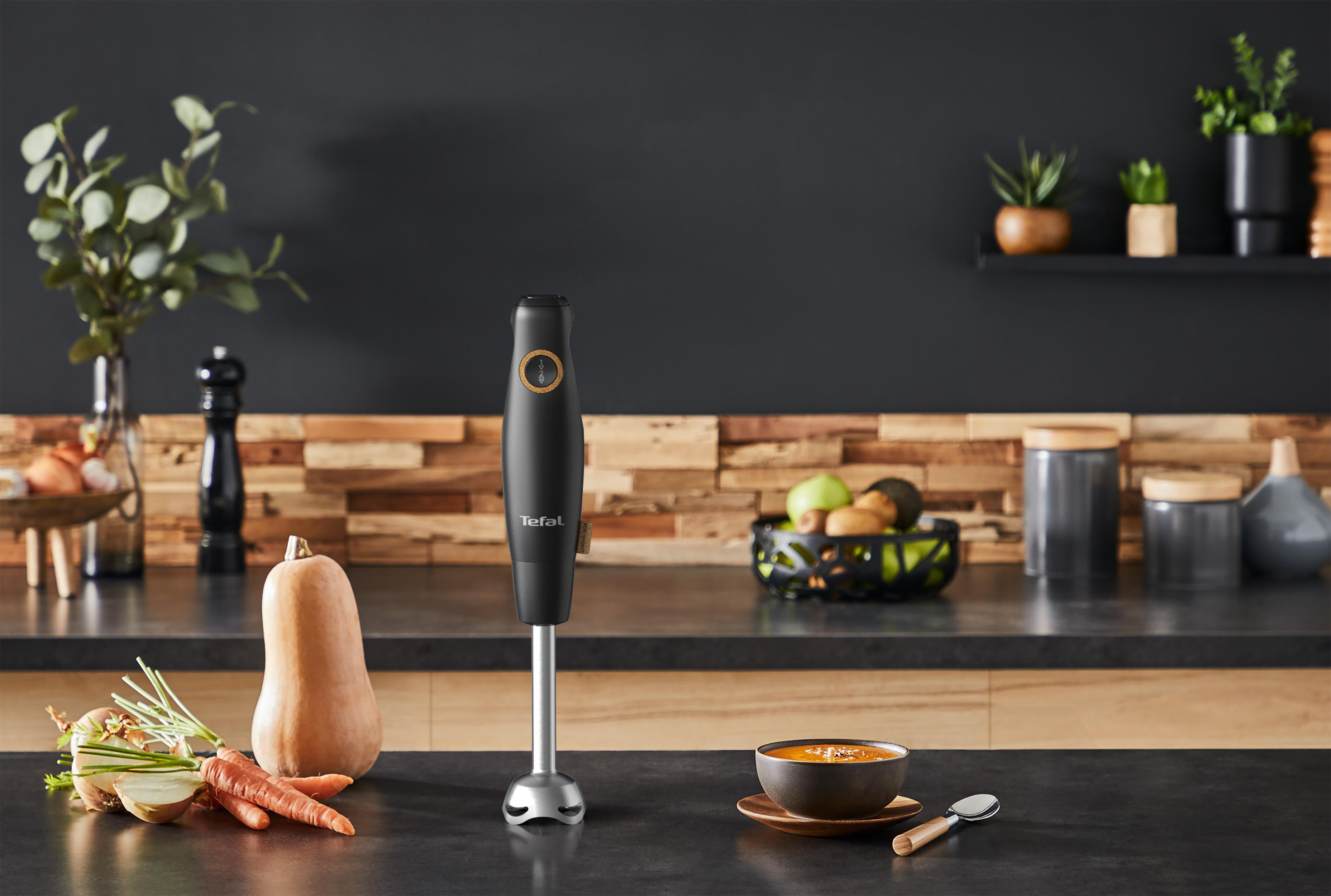 Schwarzer Stabmixer mit Gemüse, einer Schüssel Suppe auf Küchentheke.