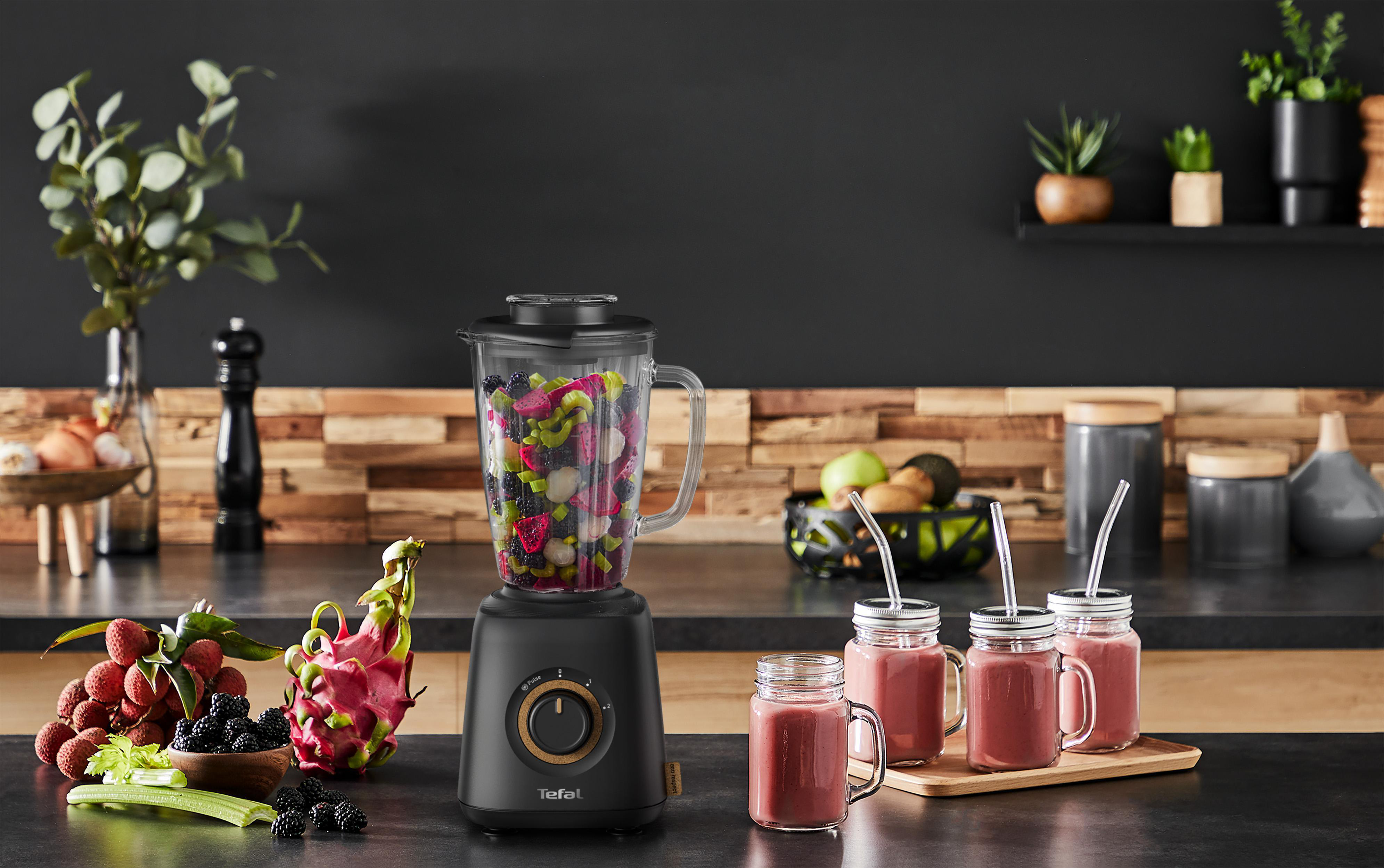 Mixer mit Früchten und Smoothies auf der Theke. Hintergrund zeigt eine Küche mit Dekorationen.