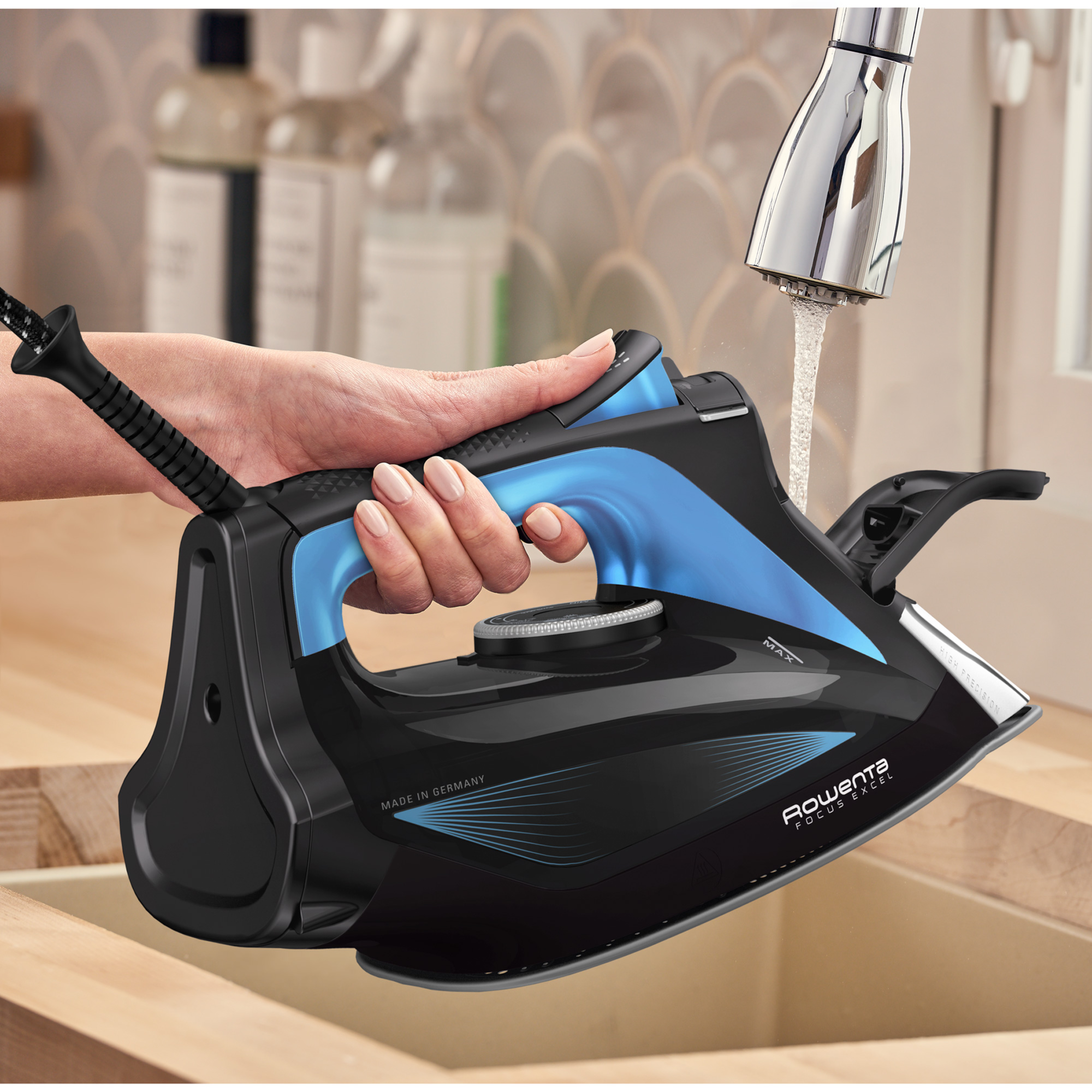 Una plancha negra y azul siendo llenada con agua en un lavabo, sostenida por una mano.