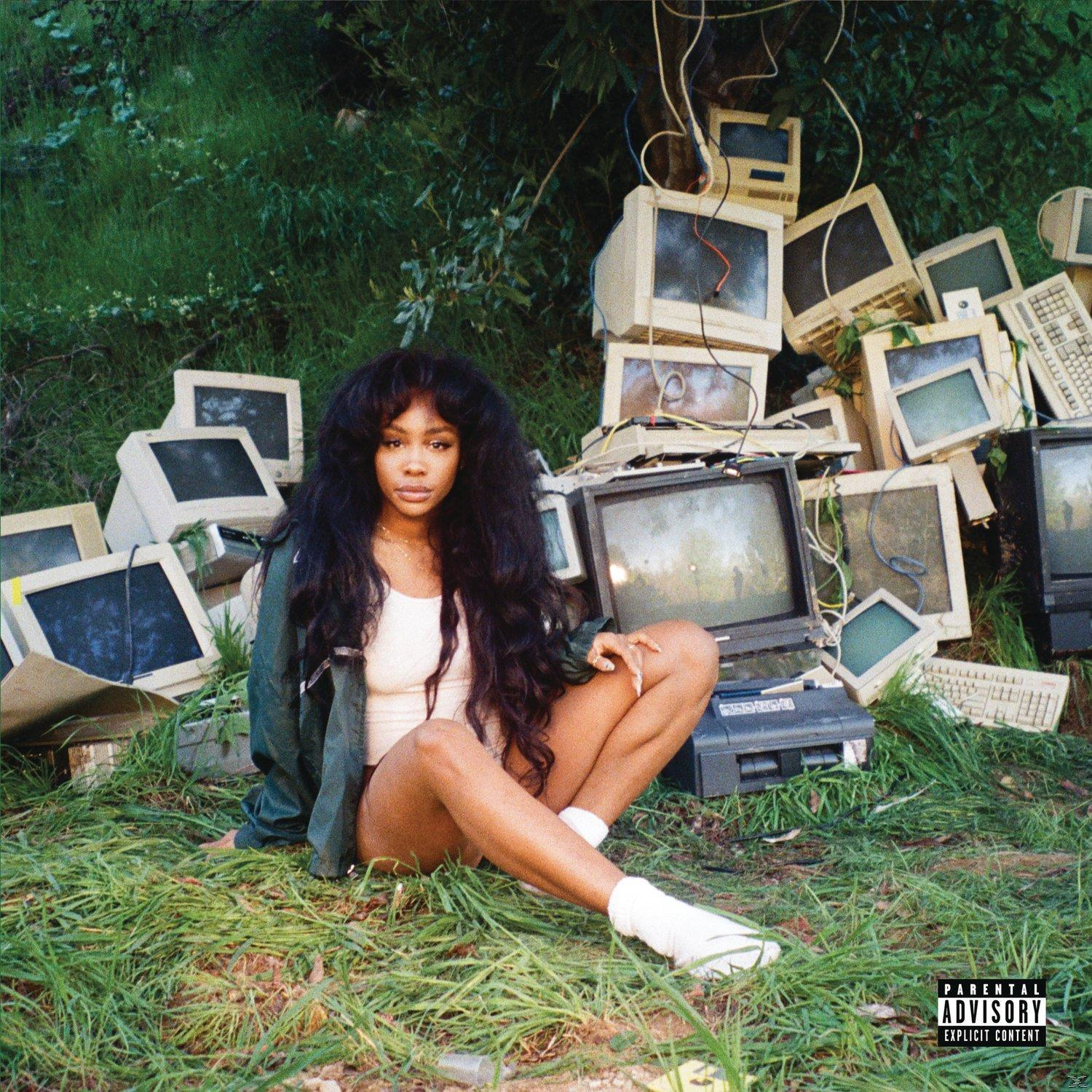 SZA régi számítógép monitorok és zöld fű között ül, fehér felsőt és zöld dzsekit visel. Parental Advisory.