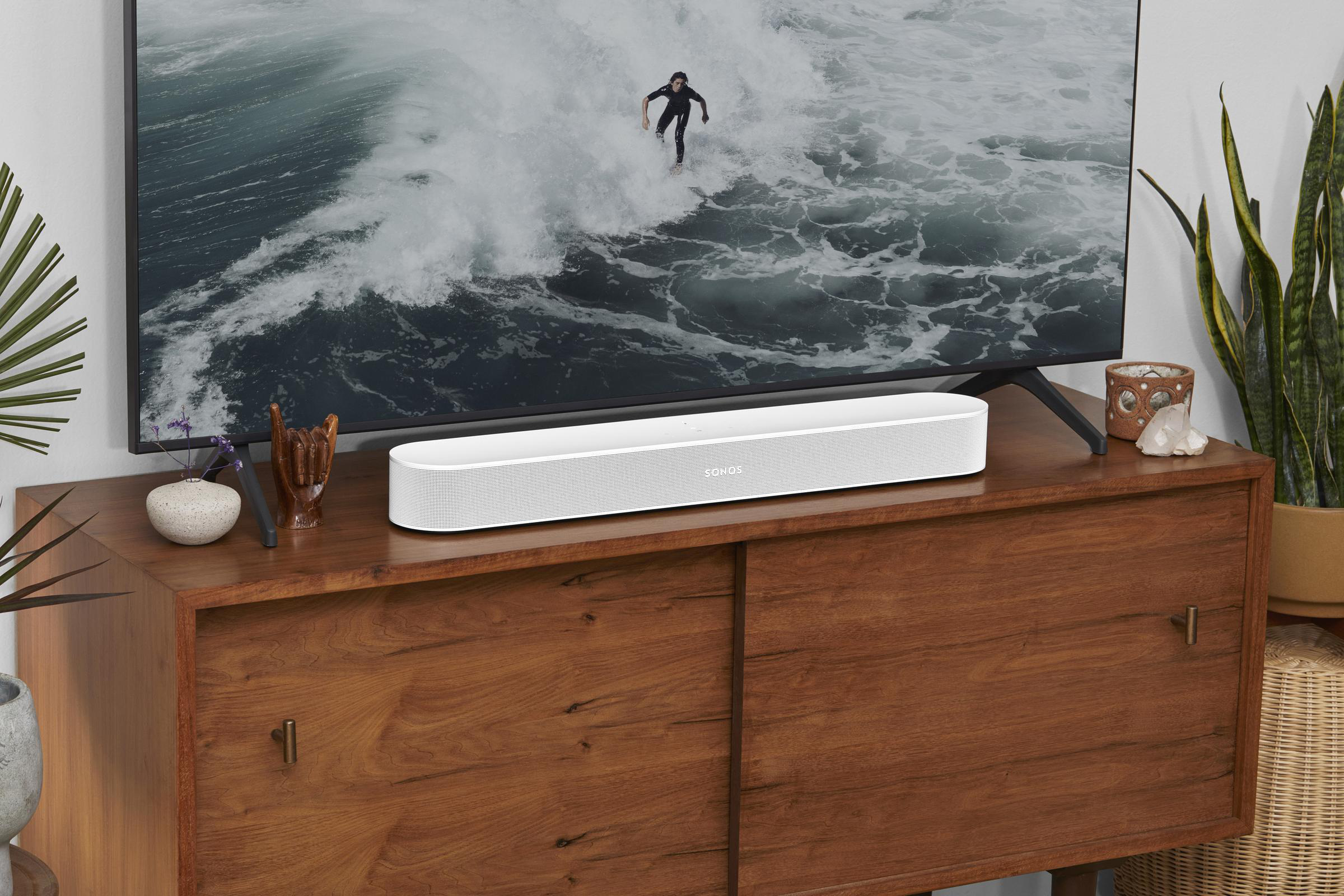 Ein Wohnzimmer mit einer weißen Soundbar auf einem Holzschrank vor einem Fernseher.