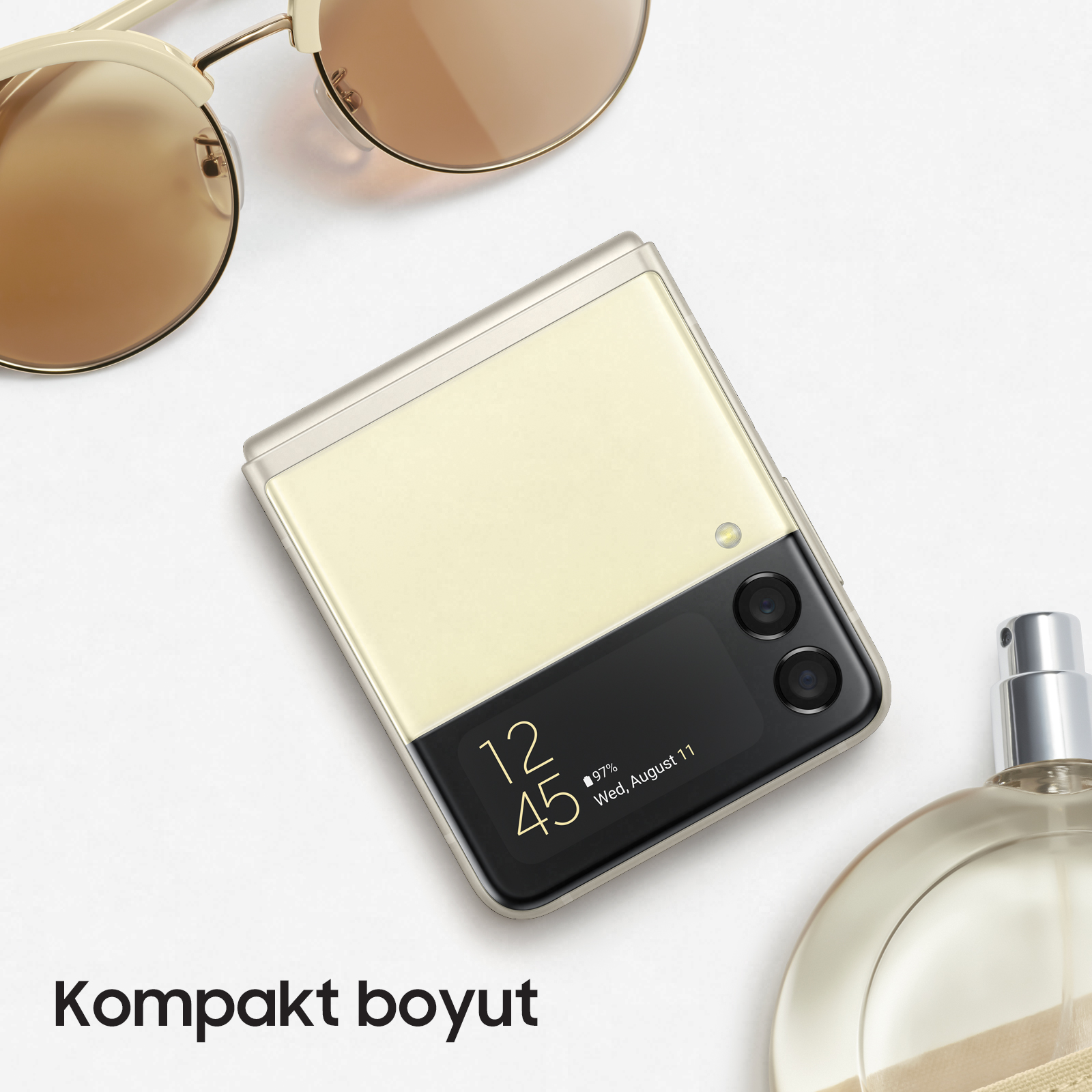Katlanabilir telefon, güneş gözlüğü ve parfüm şişesi beyaz bir yüzeyde.