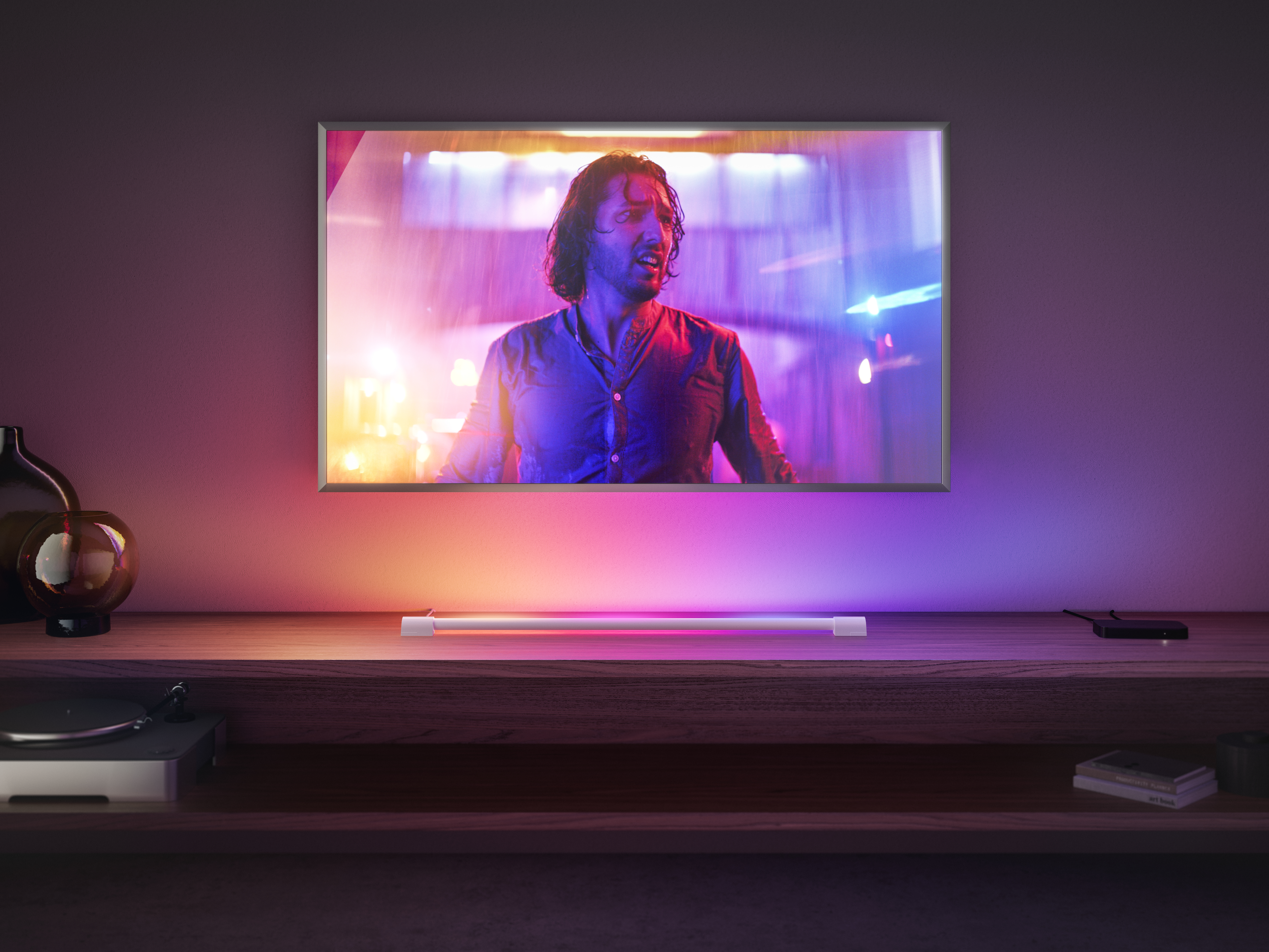 Ein Fernseher zeigt einen Mann in einer farbenfrohen Szene. Der Fernseher steht auf einem Holztisch.