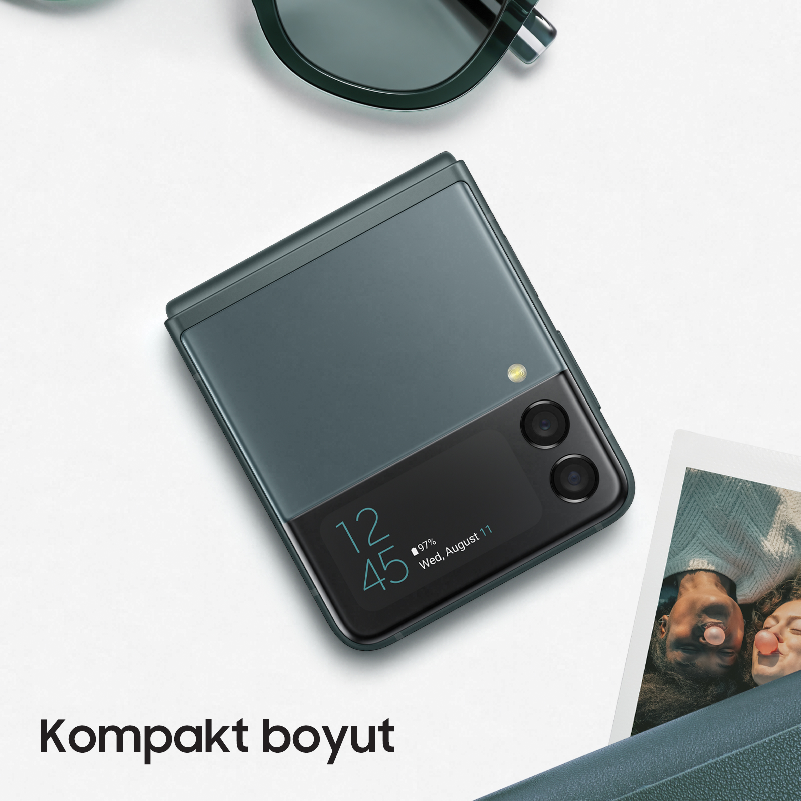 Katlanmış turkuaz telefon ve güneş gözlüğü, fotoğraf ile beyaz bir yüzeyde.