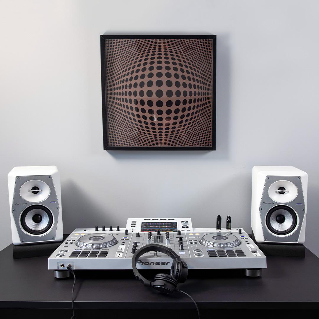 DJ-Setup mit Lautsprechern, Mischpult und Kopfhörern. Kunstwerk mit Kreisen hängt an der Wand.