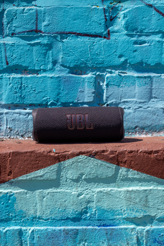Haut-parleur JBL noir sur un mur de briques rouges et bleues. De forme cylindrique.