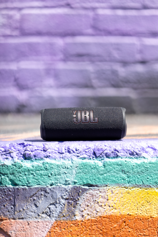 Une enceinte JBL noire sur un mur de briques multicolores. Le mur a des couleurs violettes, vertes et oranges.