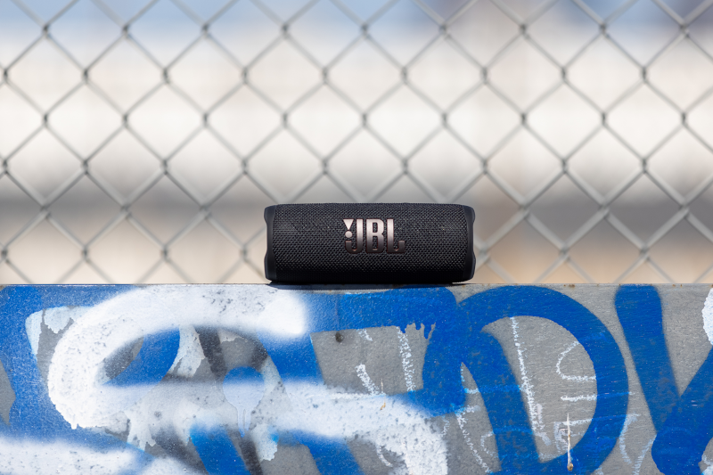 Enceinte JBL noire sur une surface en béton avec graffiti, avec une clôture en treillis métallique en arrière-plan.