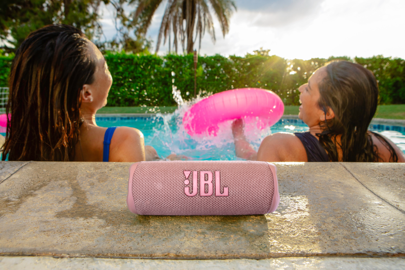 Deux femmes dans une piscine, un haut-parleur JBL rose repose sur le bord.